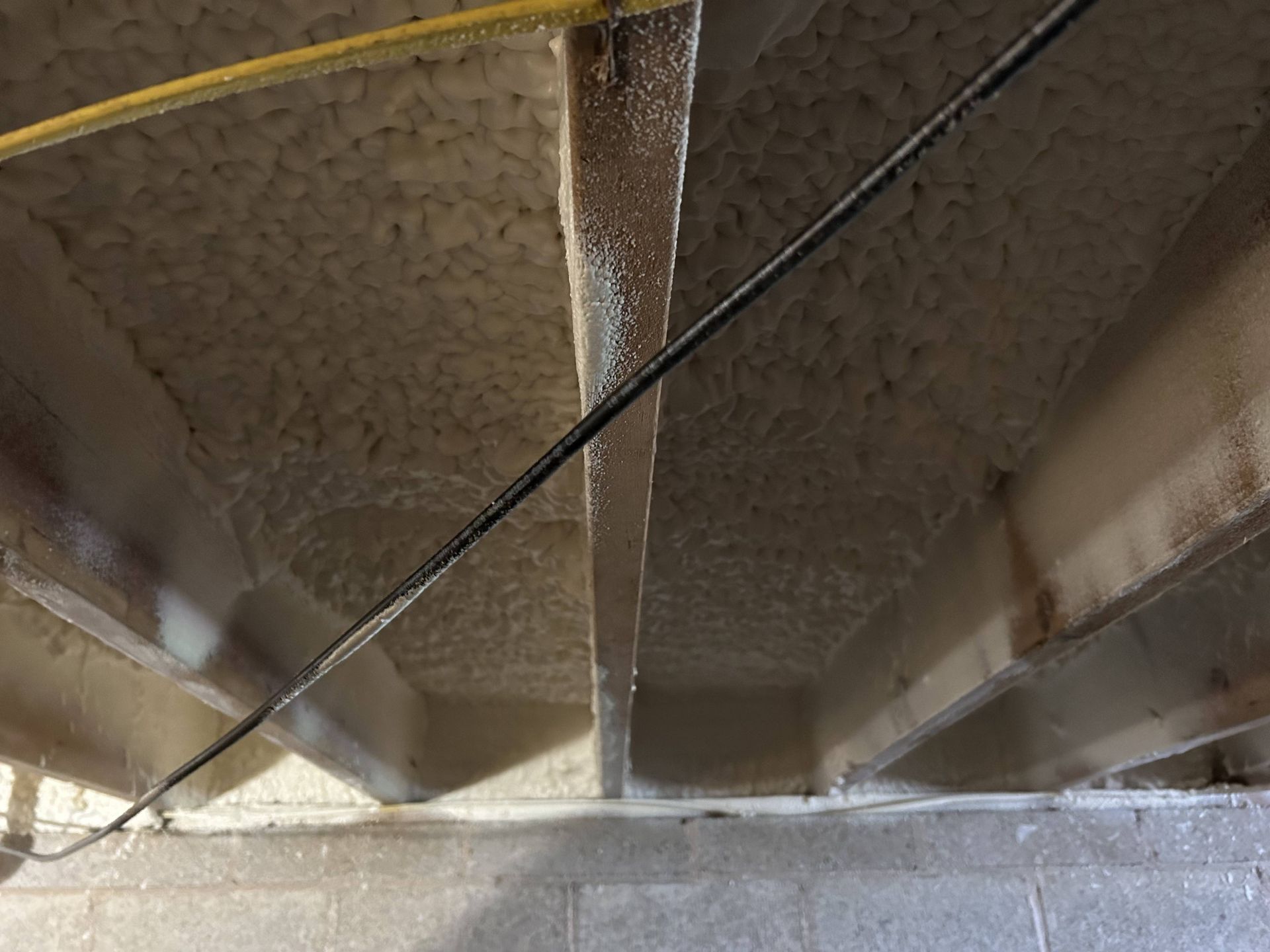 Interior view of attic insulation with ducts and a cable running diagonally across the frame