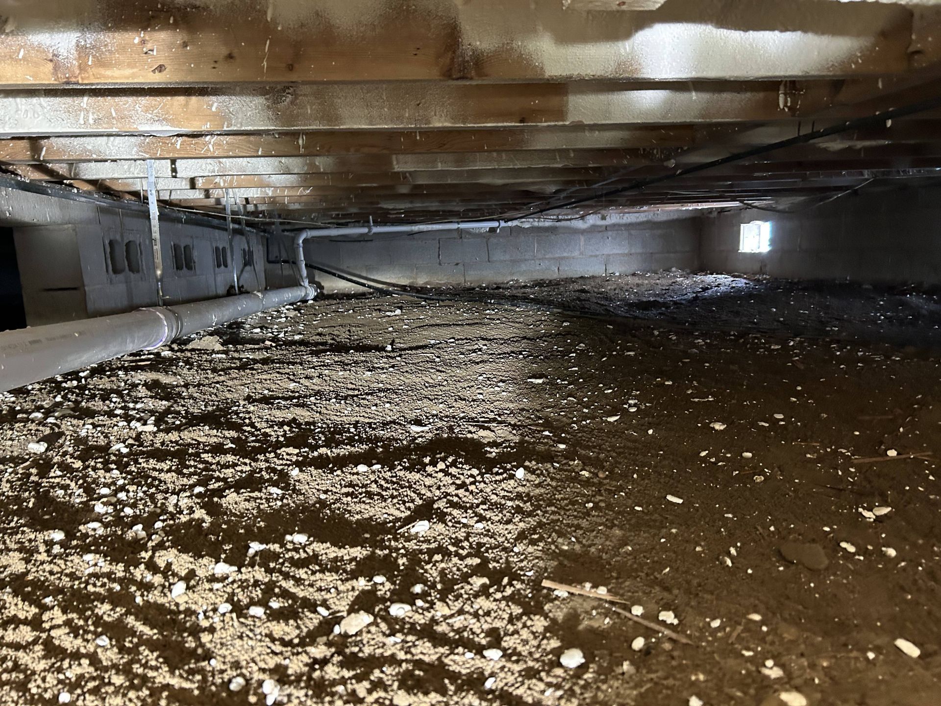 Flooded crawlspace with muddy water, low ceiling beams, and debris scattered across the floor.