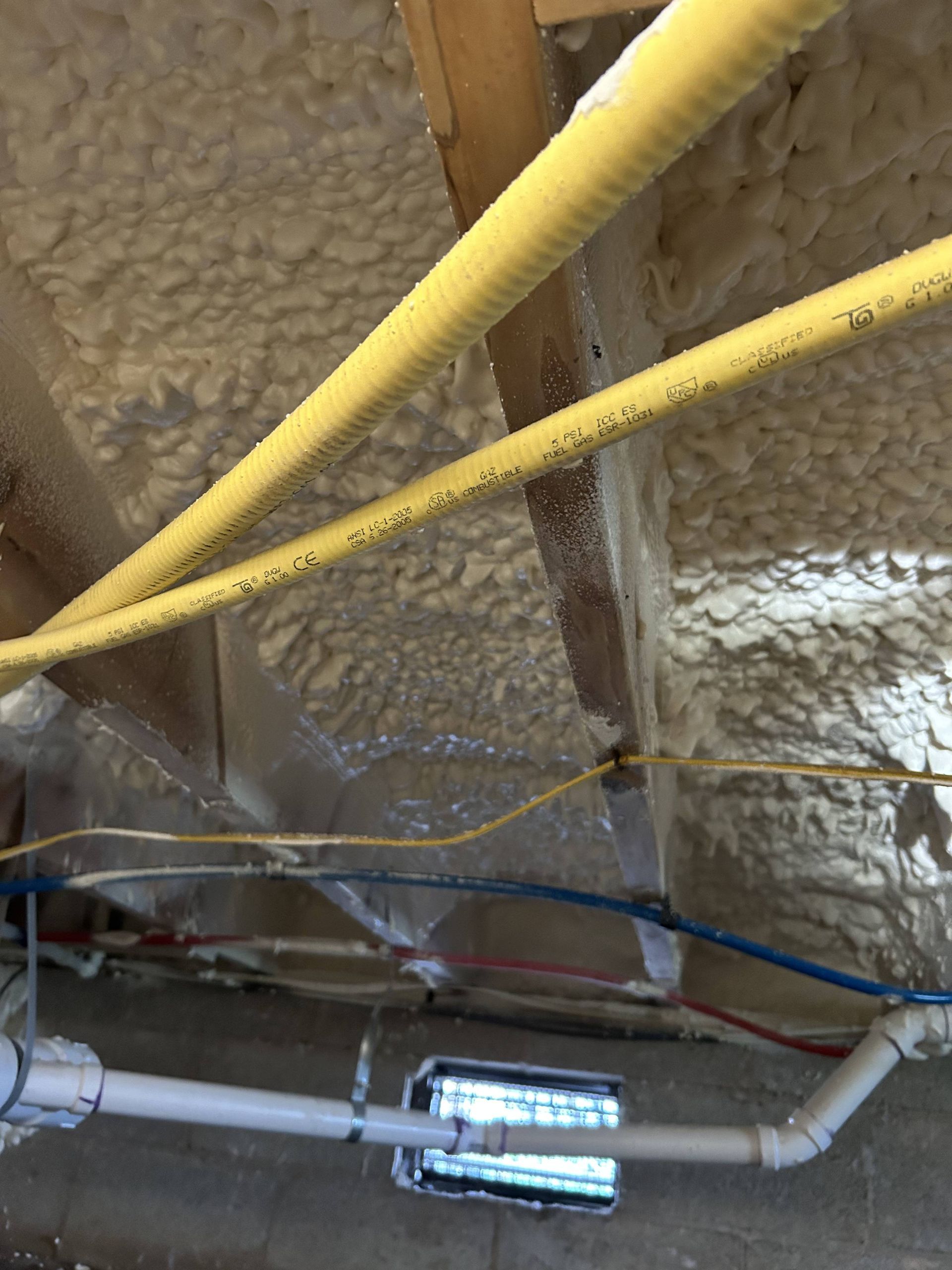 Insulated ceiling ductwork and pipes with yellow and gray pipes running across an unfinished attic space
