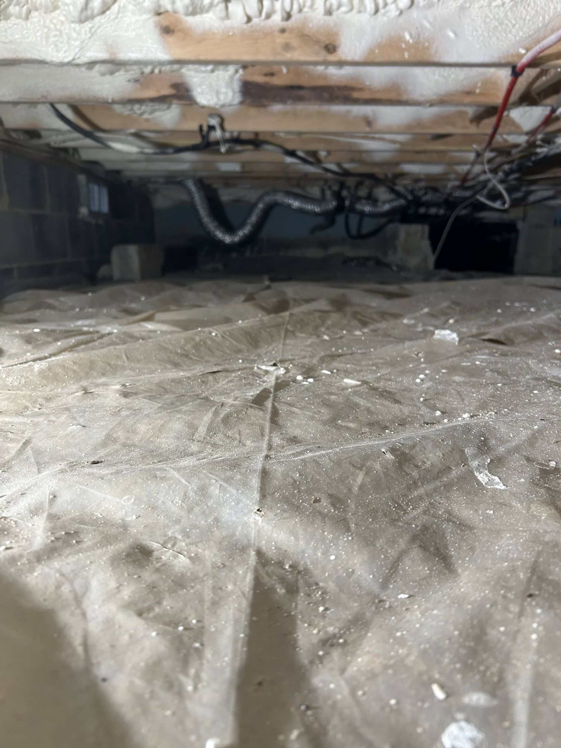 Crumpled white insulation in a crawlspace with exposed wiring and wooden joists overhead.