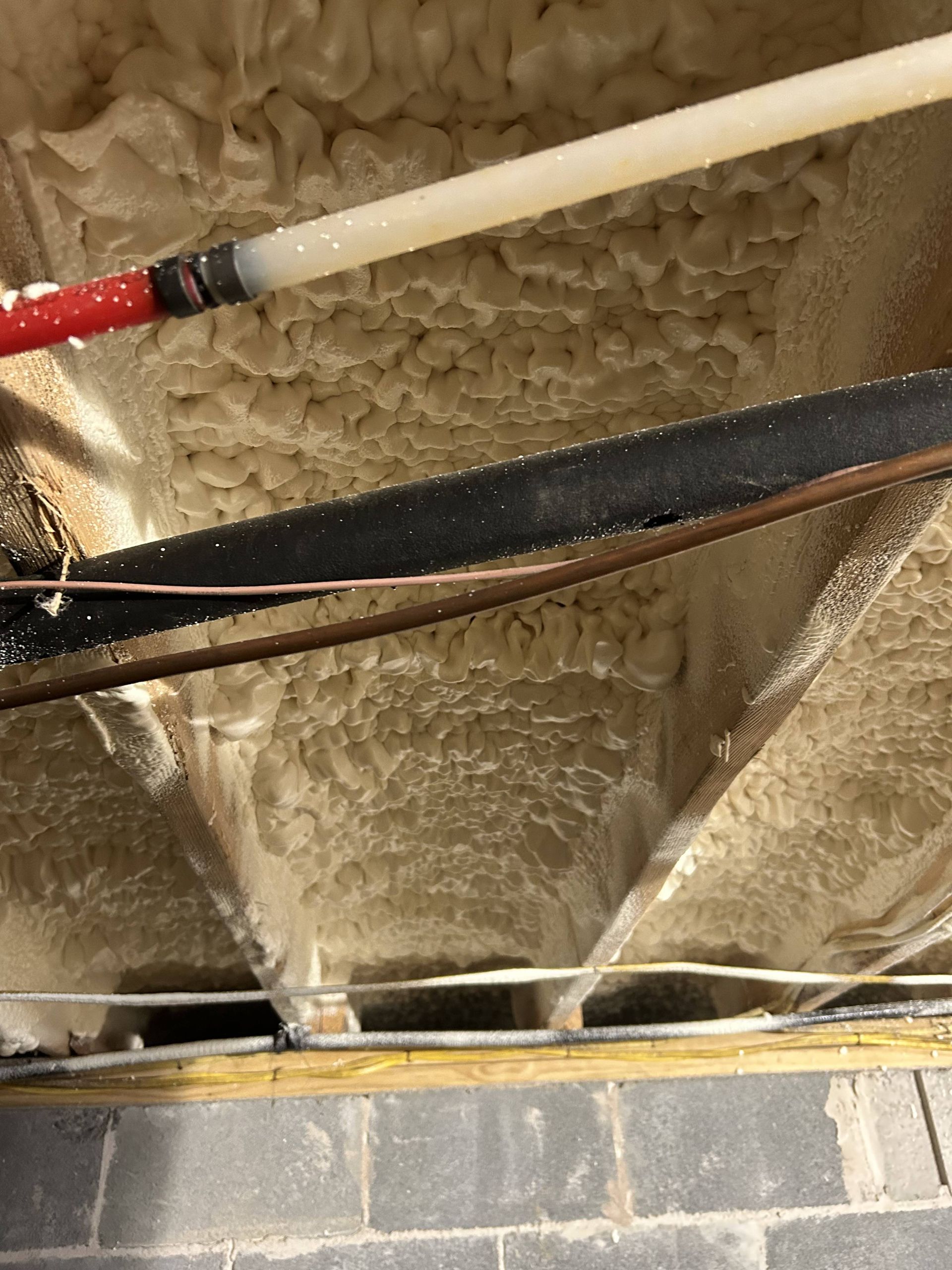 Ceiling insulation with exposed pipes and wires above a cinder block wall
