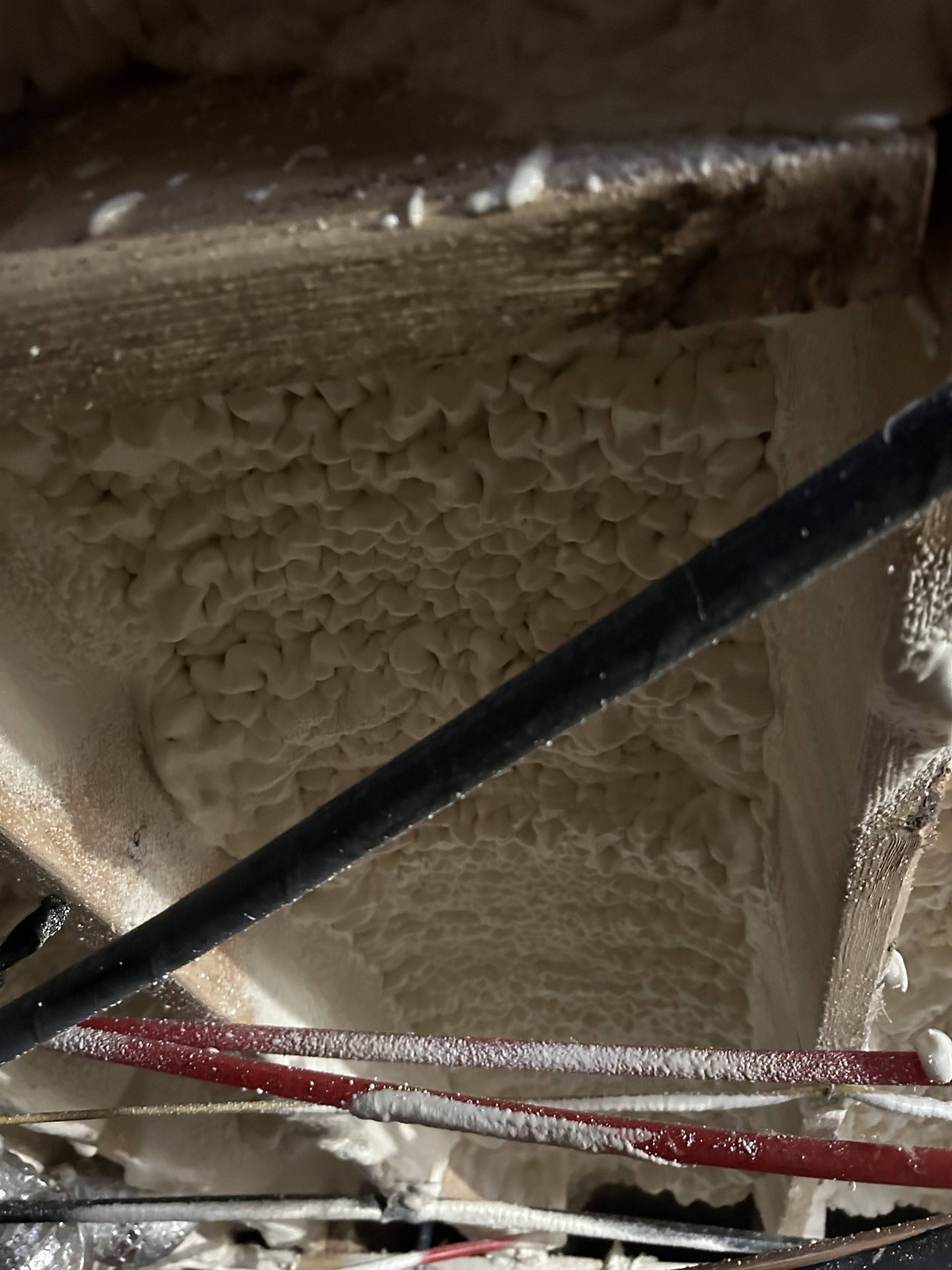 Close-up of beige insulated ceiling cavity with black and red cables crossing underneath