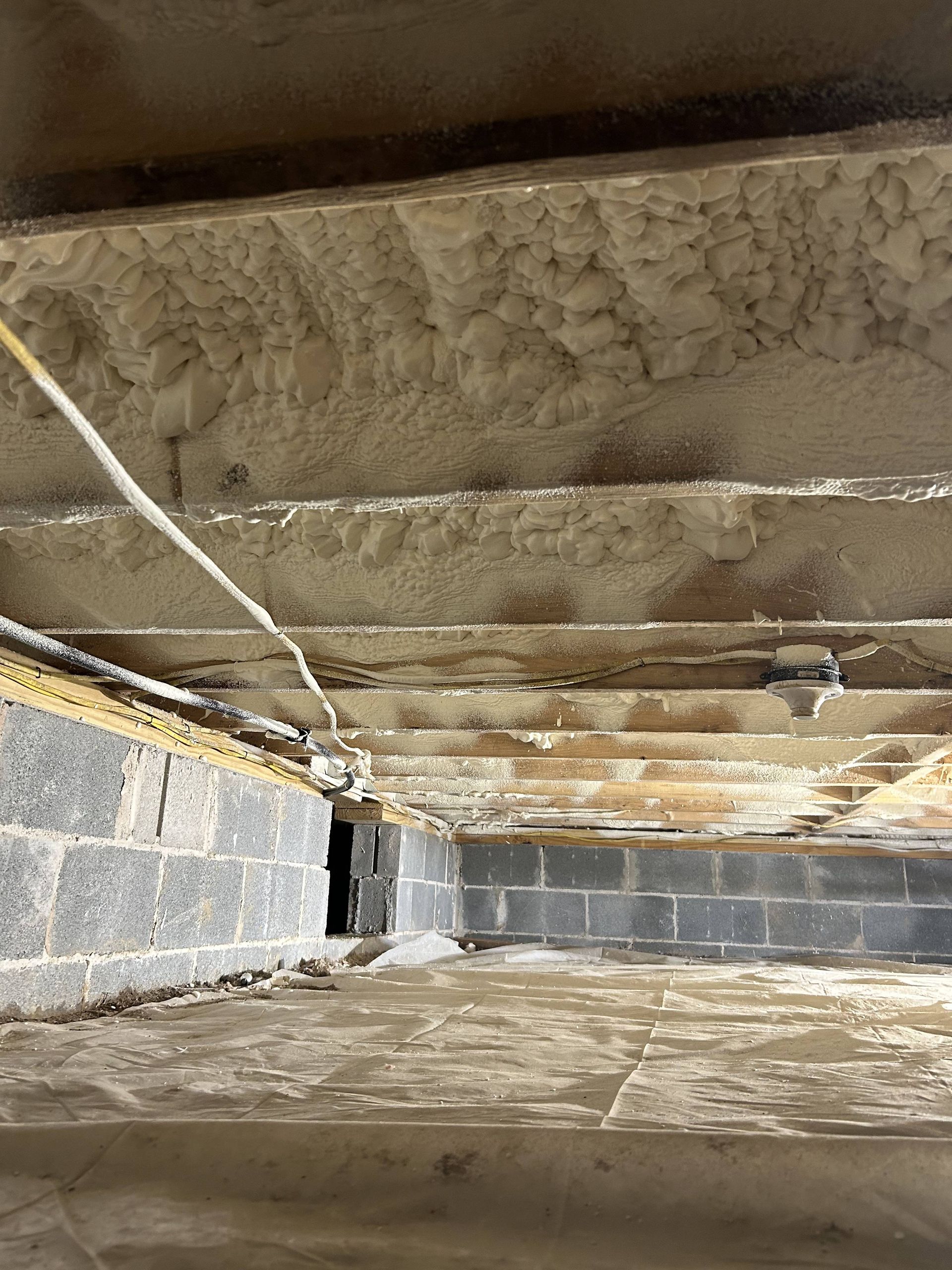 Crawlspace with exposed wooden joists and insulation above a cinder block foundation wall