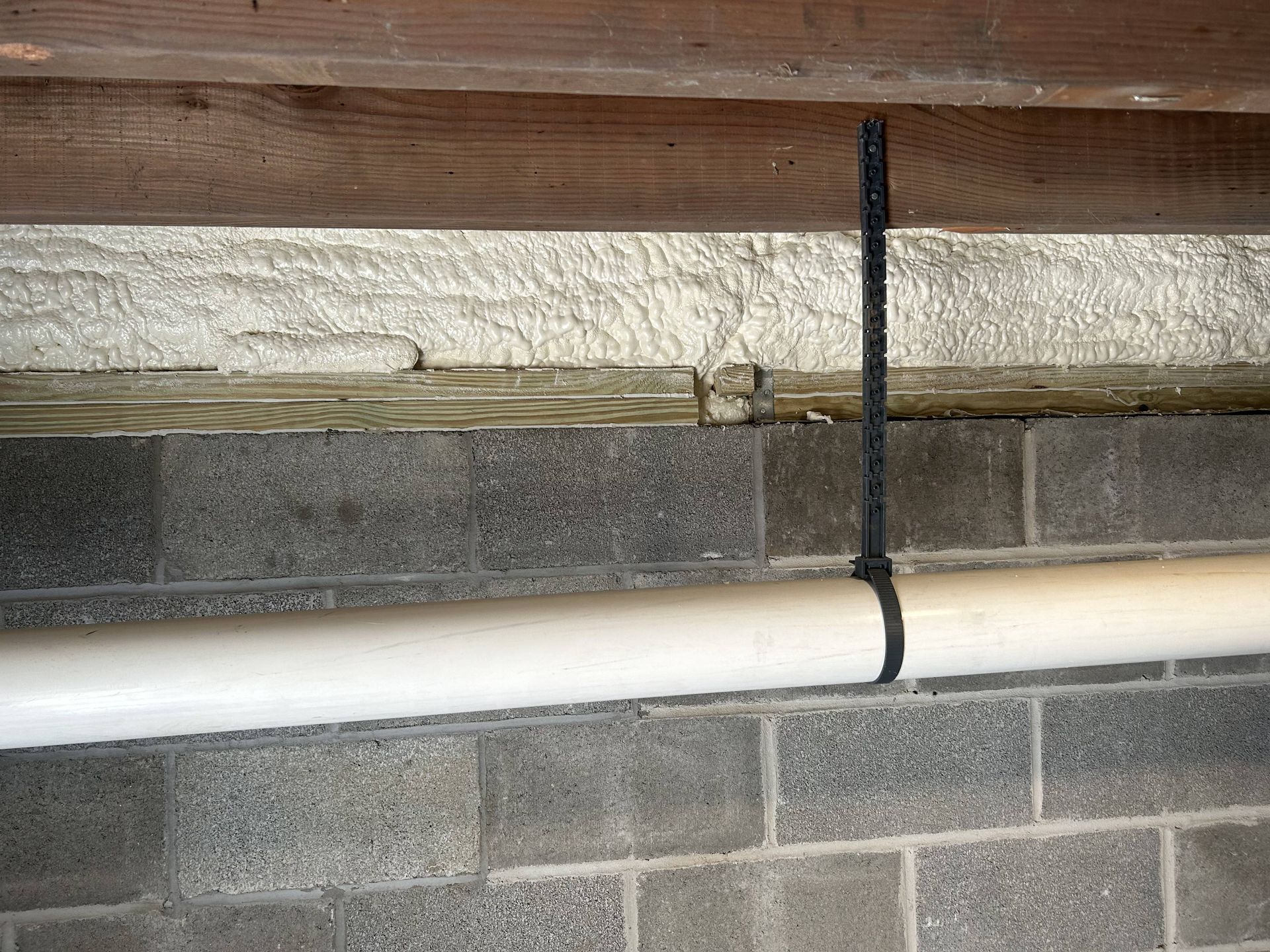 Pipe strapped to cinder block wall beneath a wooden beam