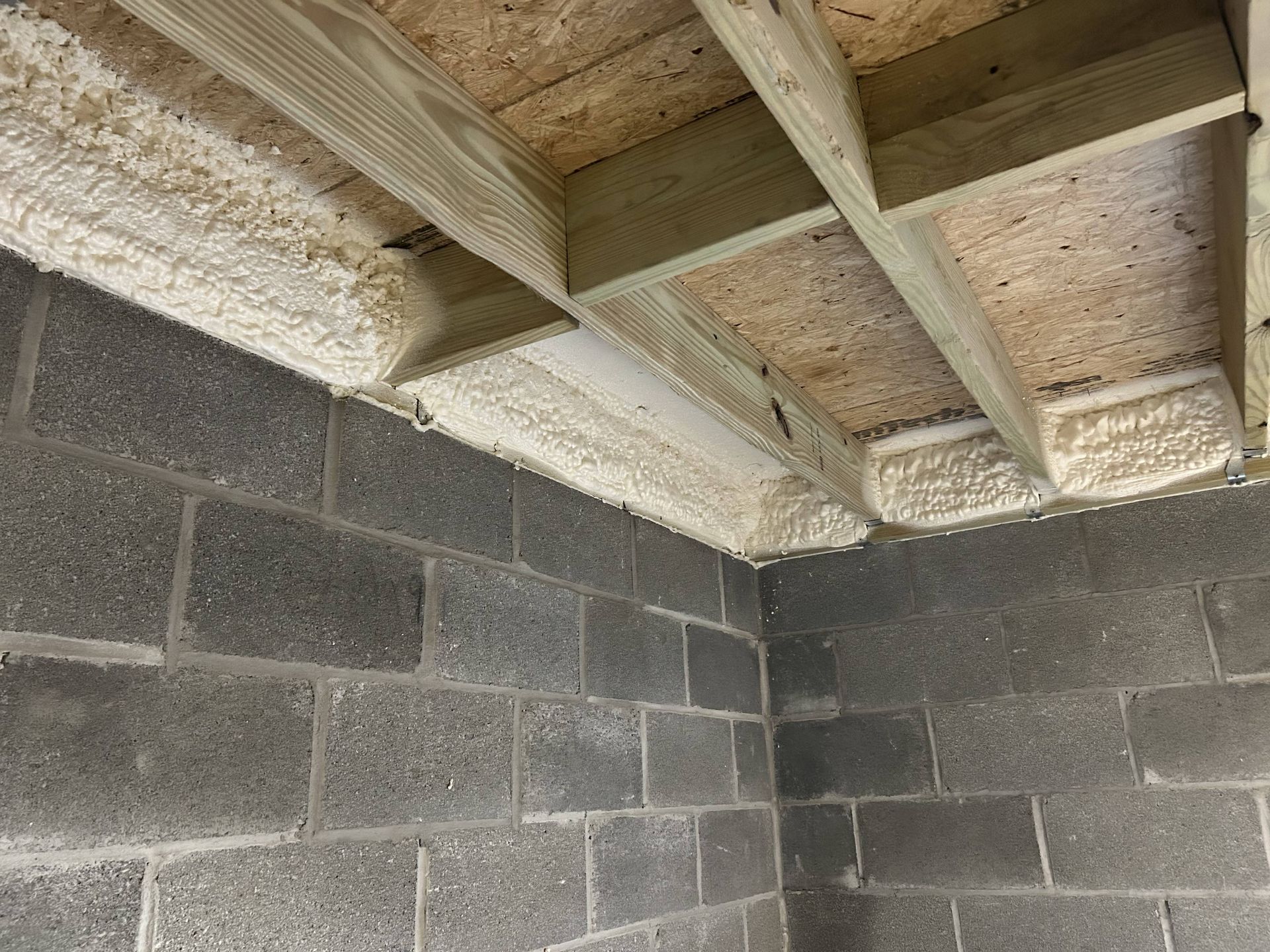 Interior corner of a cinder block room with exposed wooden ceiling joists and insulation