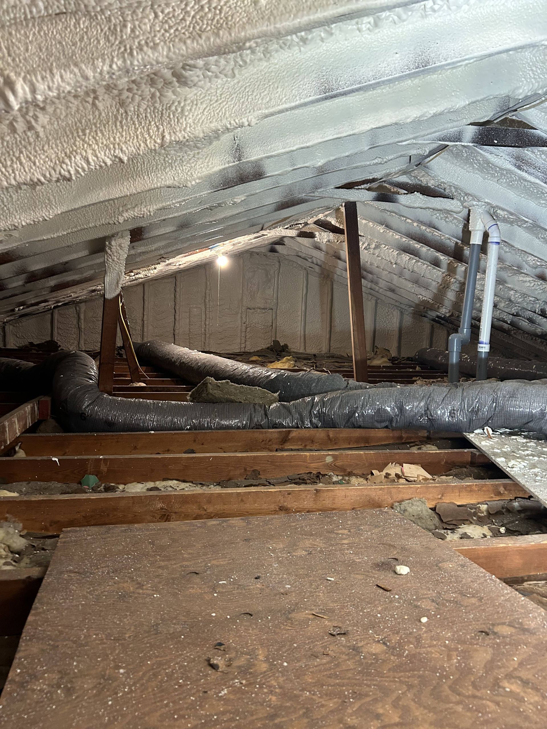 Crawlspace with exposed beams, insulation, and wooden joists under a damaged floor.