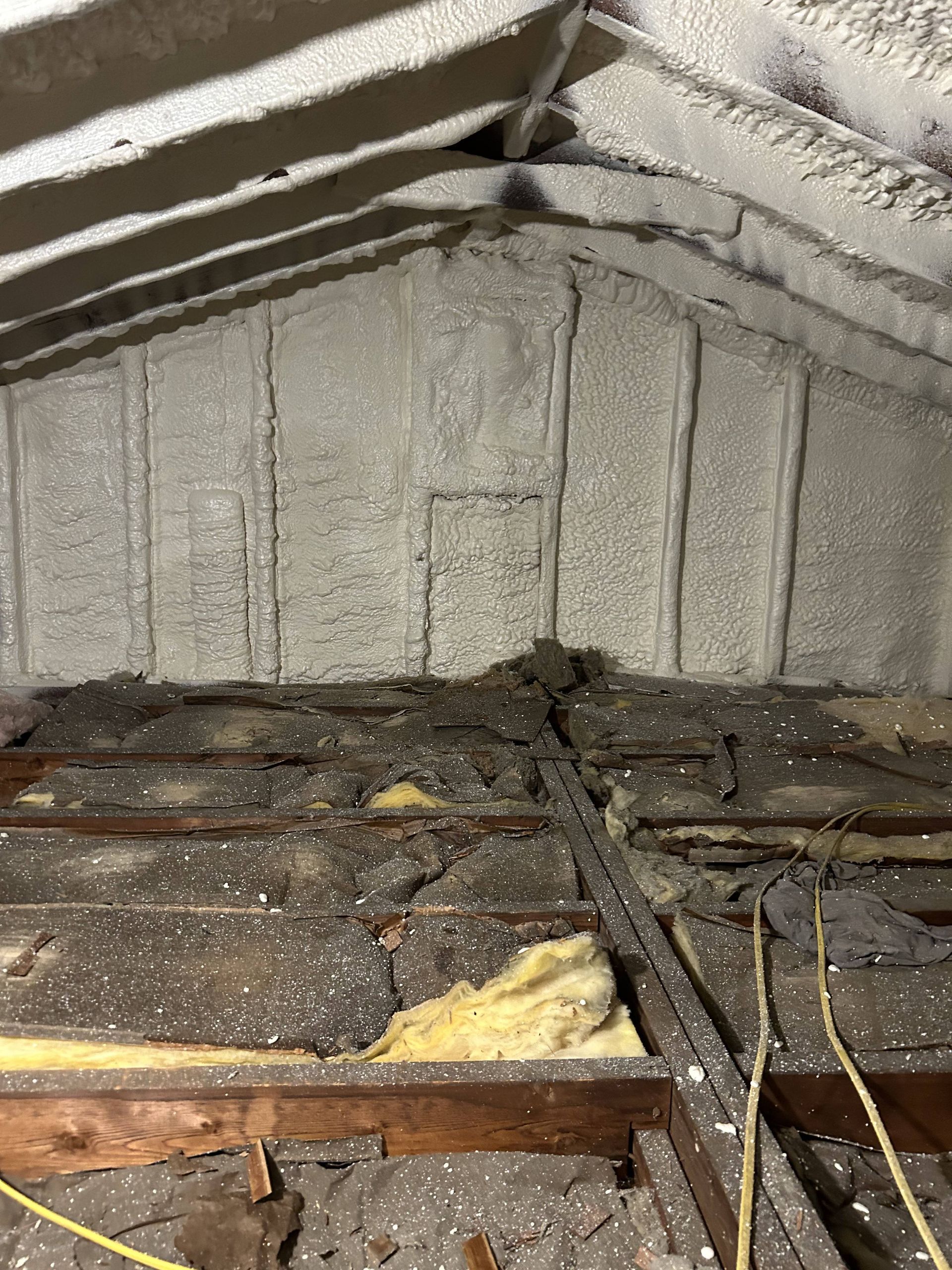 Damaged attic with insulation, exposed wooden beams, and debris on the floor