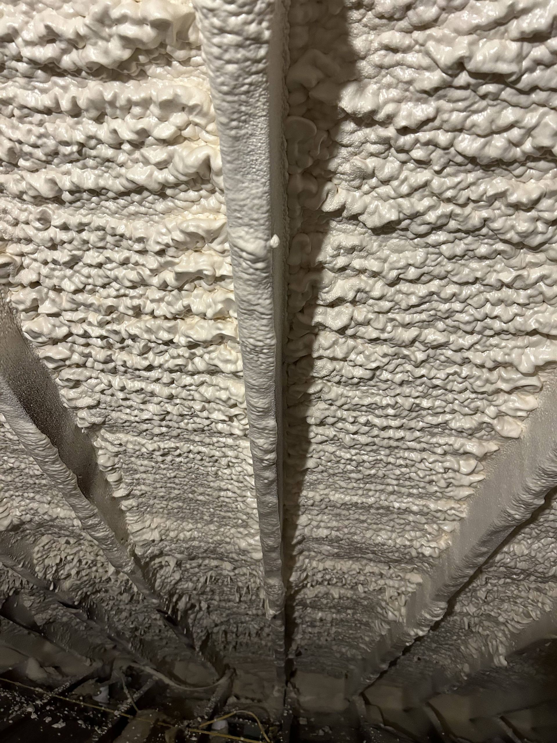 Foam insulation sprayed between exposed roof rafters in an attic space.