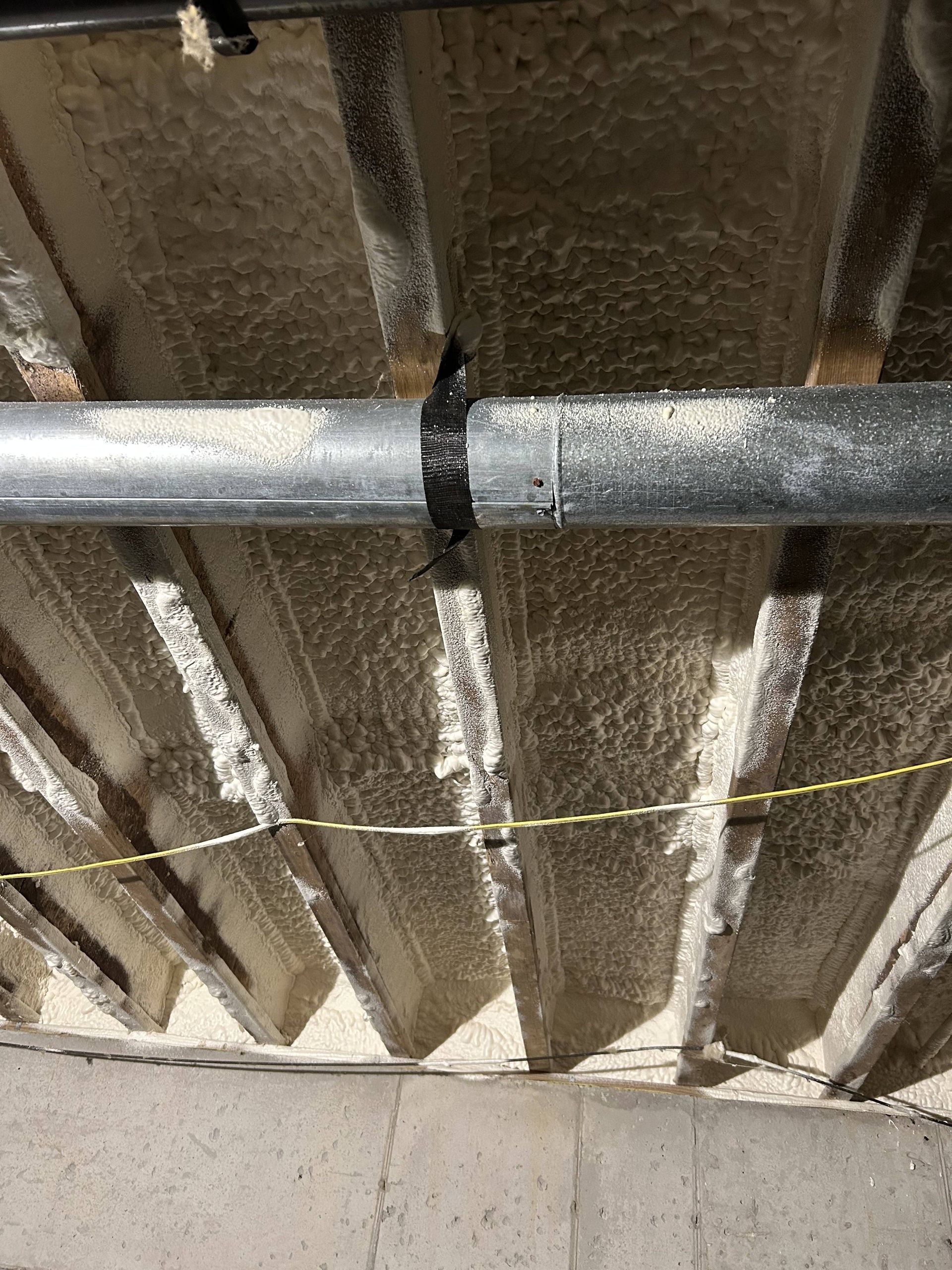 Ceiling with exposed pipes and beams, including a black pipe connection and yellow cord below.