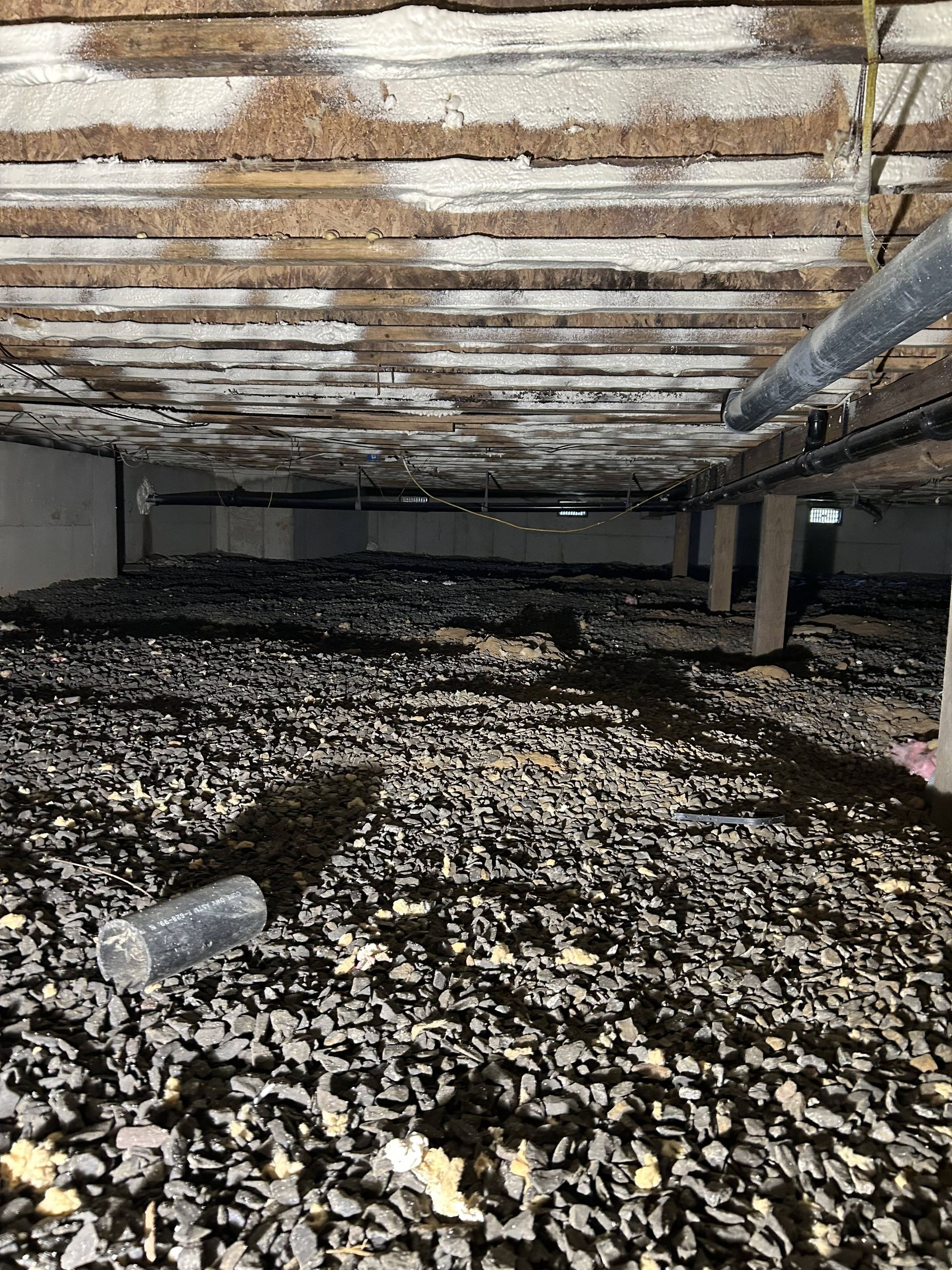 Flooded crawlspace with low beams, moldy insulation, and debris-covered ground