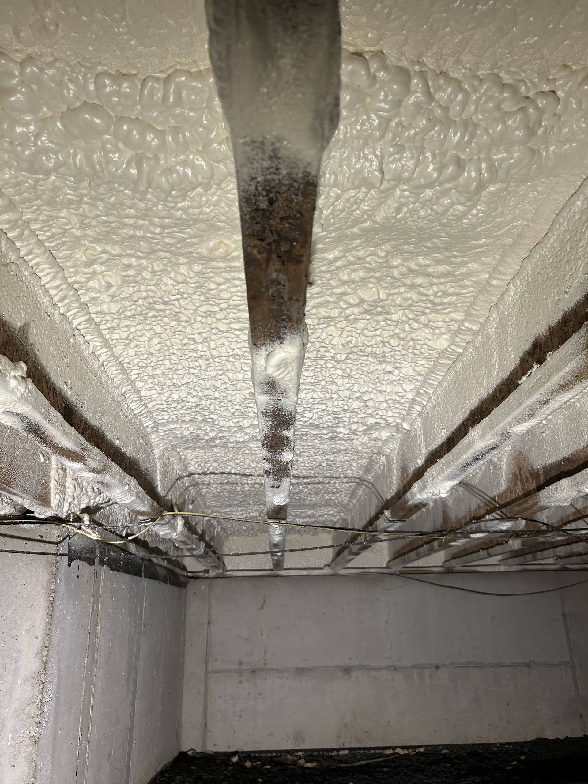 Insulated basement ceiling with spray foam and exposed pipes and wiring
