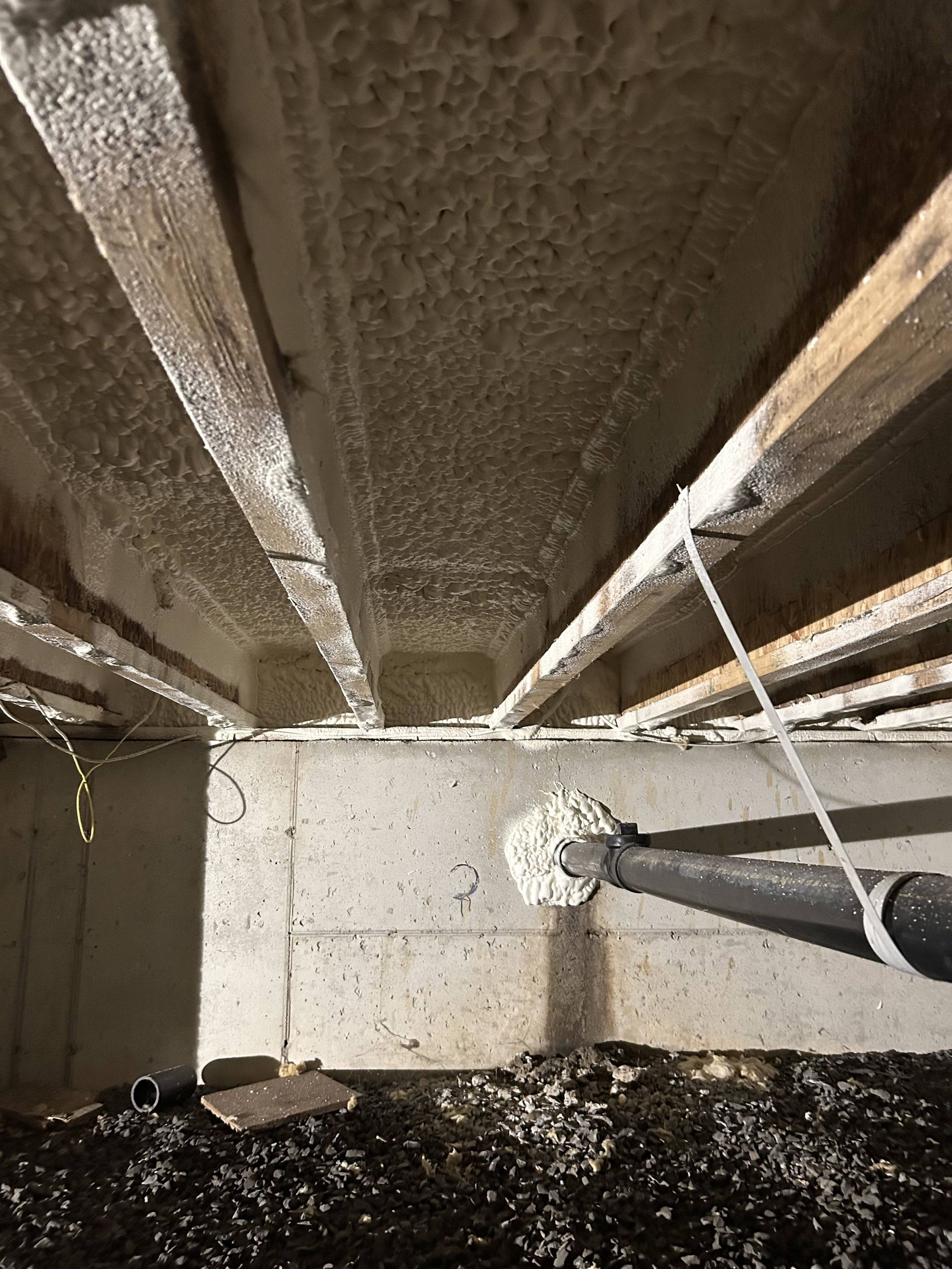 Person spraying foam insulation onto basement ceiling joists