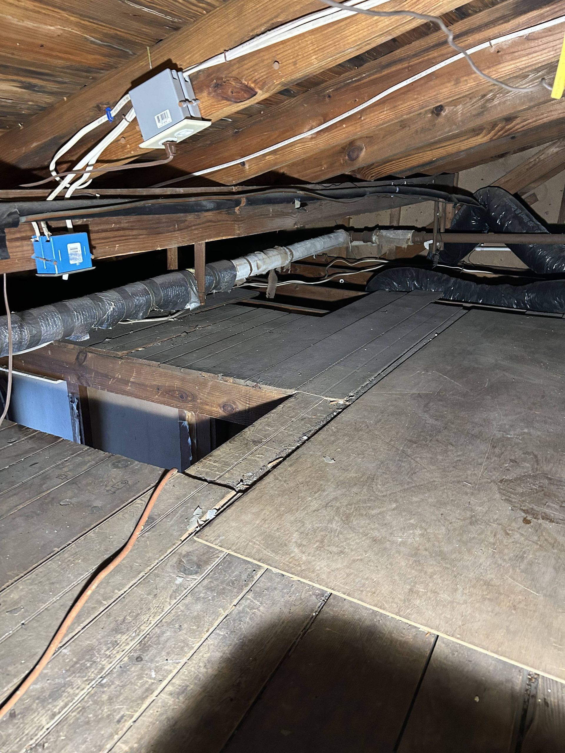 Damaged attic floor with missing boards, exposed beams, and electrical boxes under slanted wooden rafters