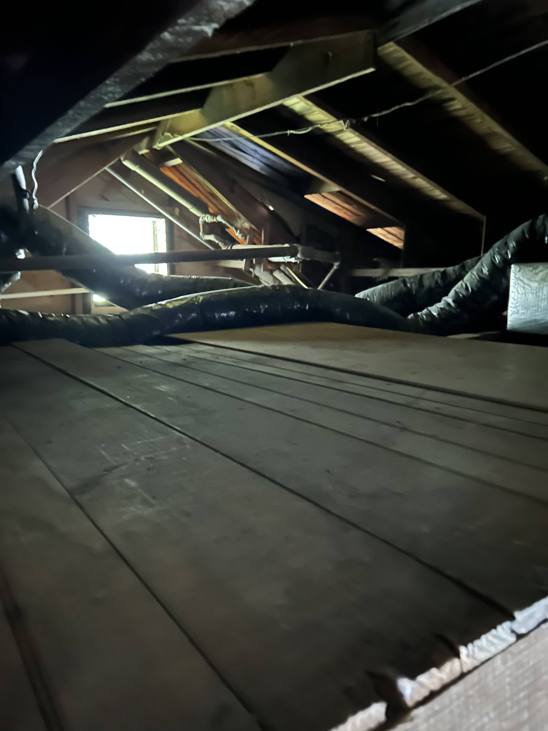 Dark attic with exposed rafters, wood floorboards, and daylight from a small window.