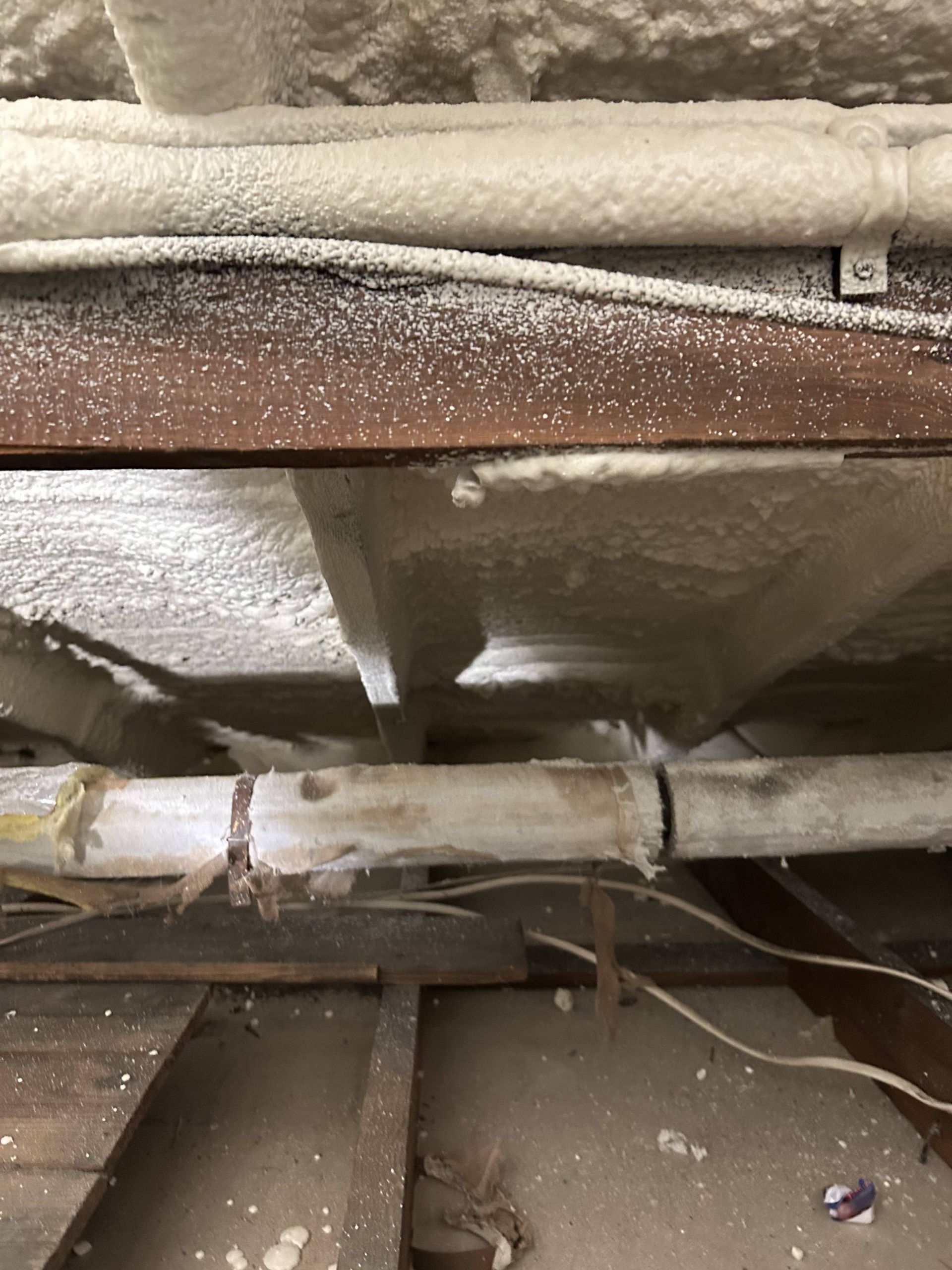 Dusty crawlspace with exposed pipes, beams, and insulation under a wooden floor