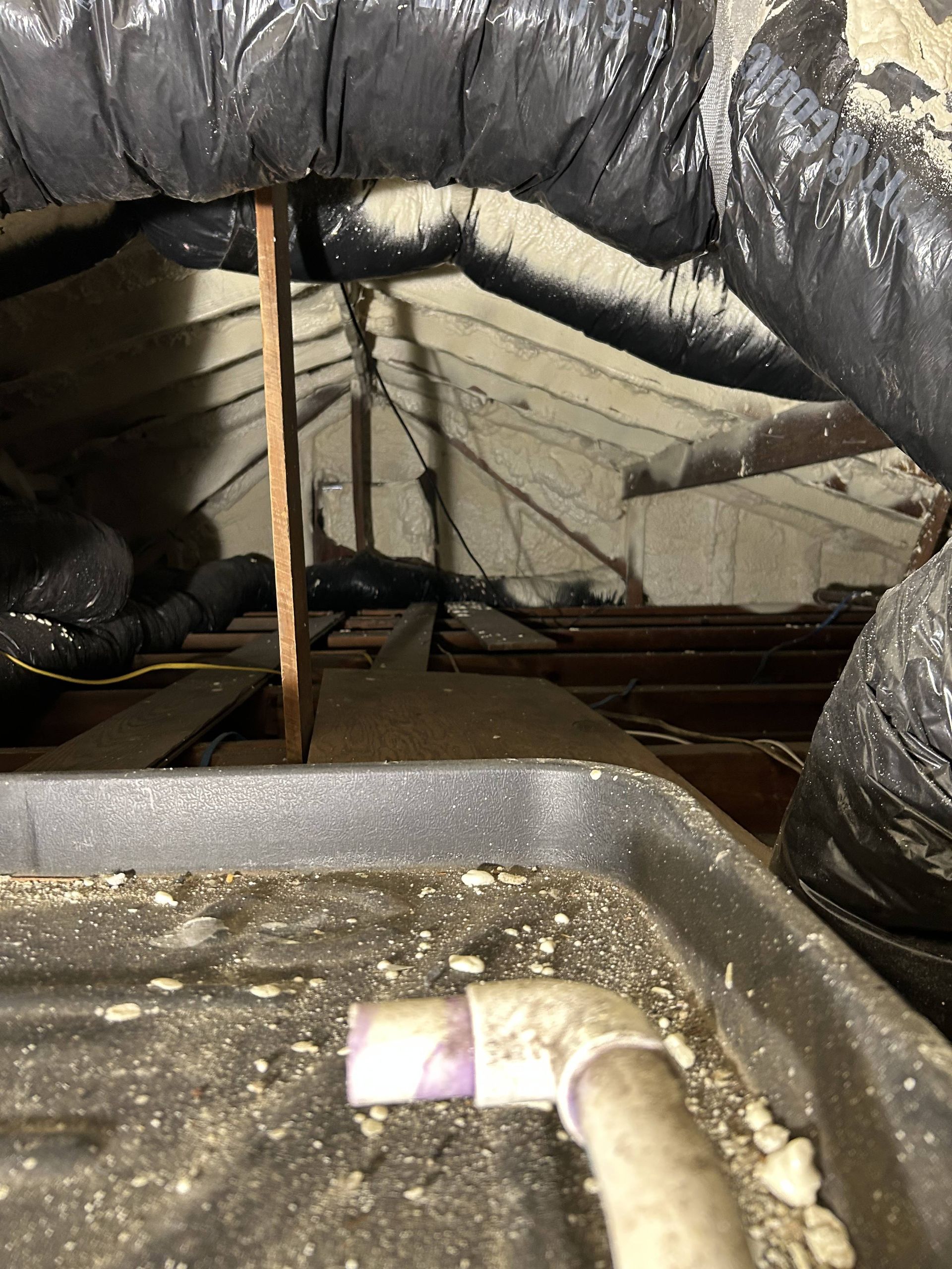 Insulated attic with black ductwork, exposed beams, and a utility pipe in the foreground.