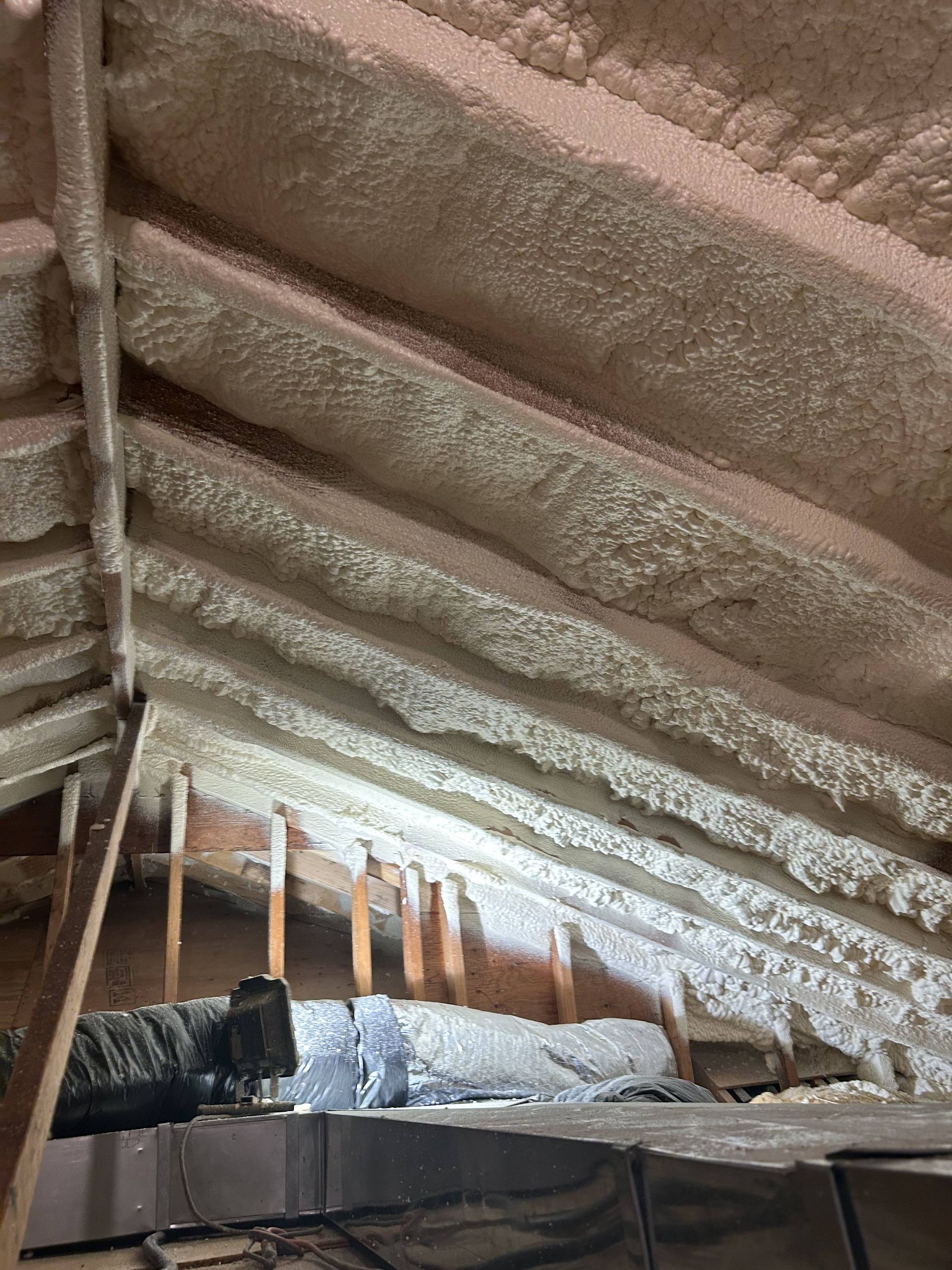 Attic with spray foam insulation on sloped rafters and exposed wooden beams
