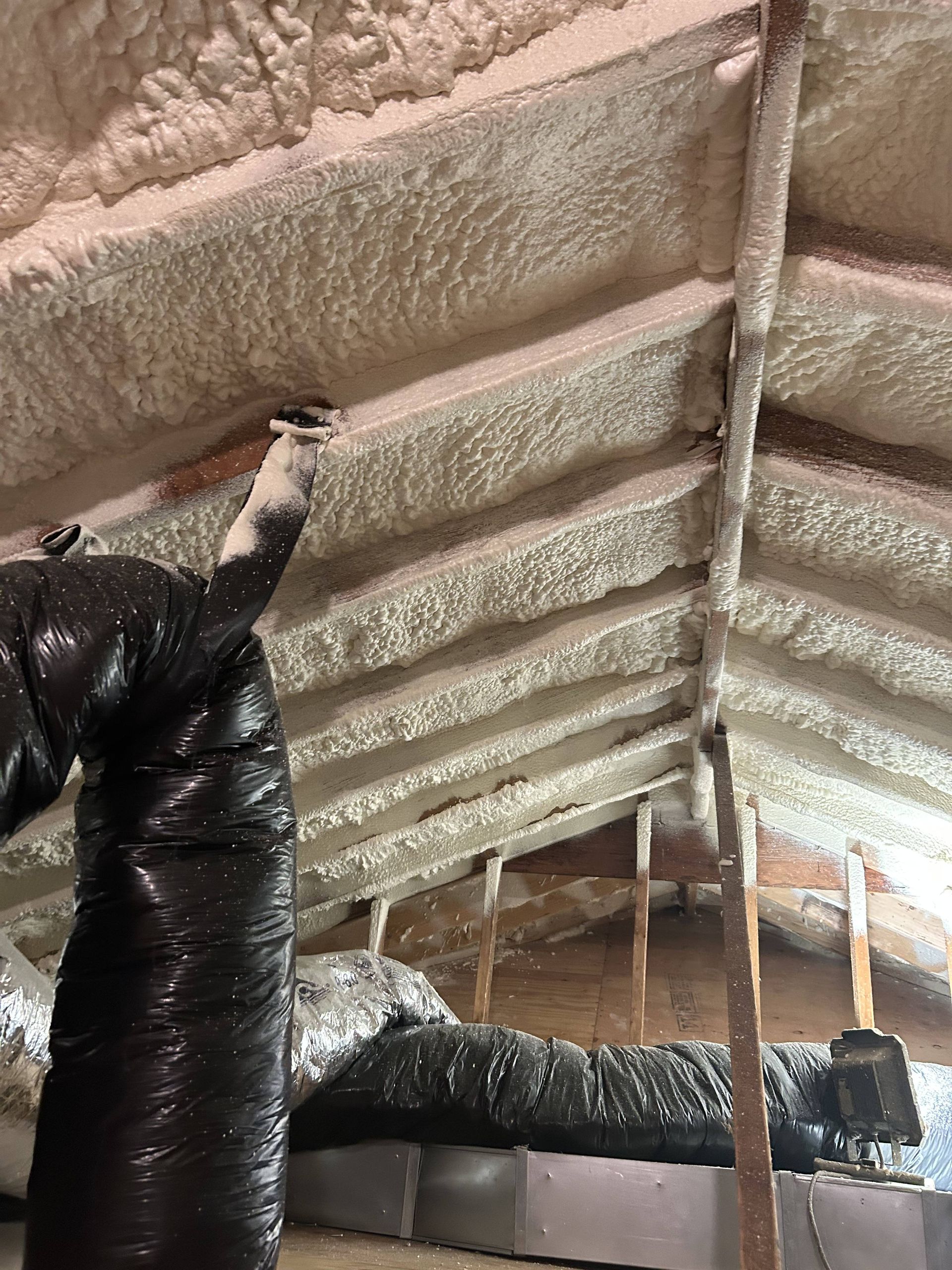 Insulated attic ceiling with exposed beams, black ductwork, and a light fixture hanging from the rafters.