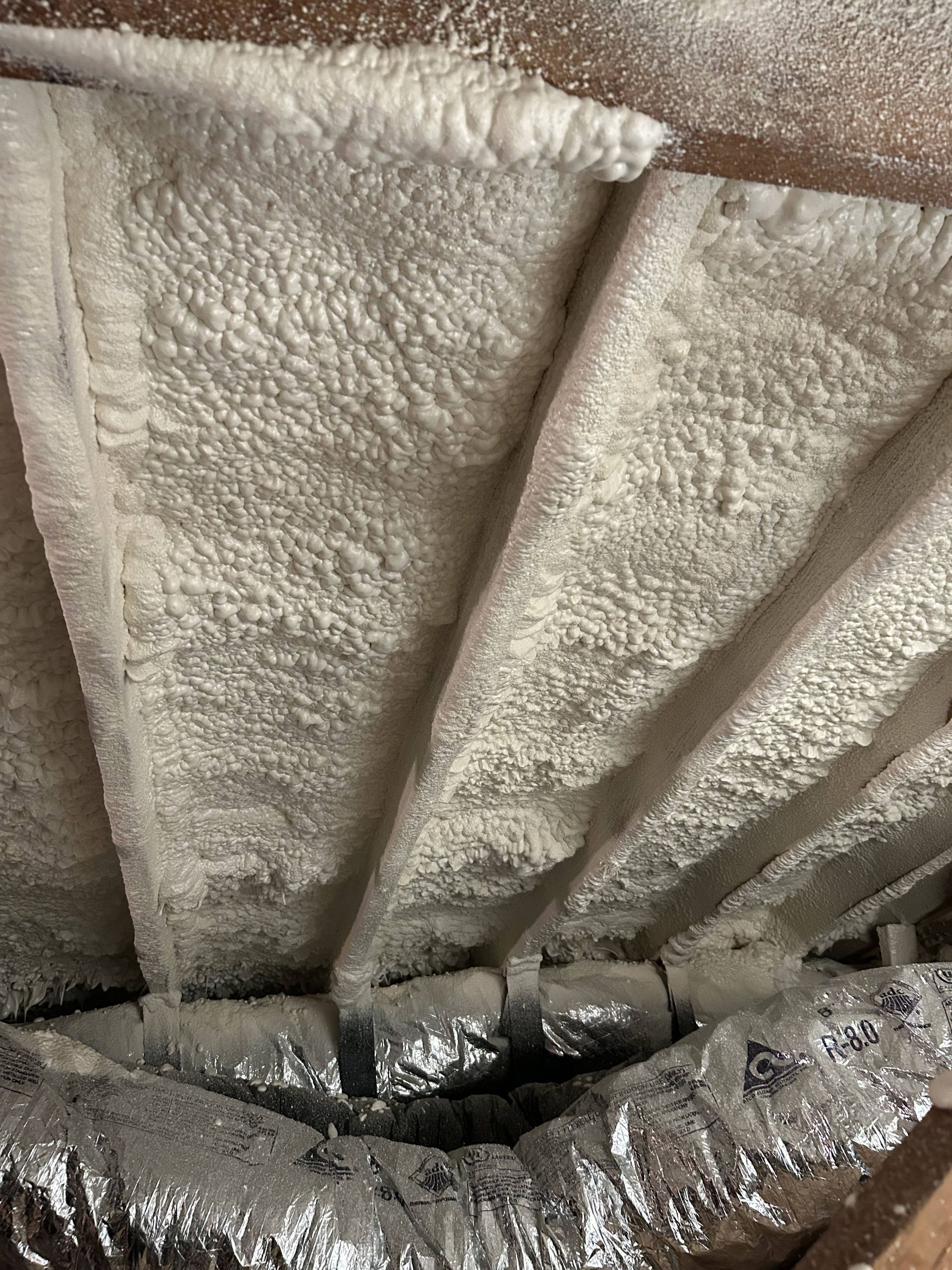 Close-up of a cream-colored textured ceiling with visible rafters and a silver duct below