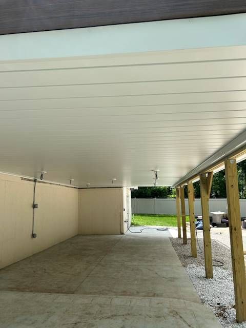 Covered concrete patio with white ceiling, beige wall, and wooden posts opening to a grassy yard.