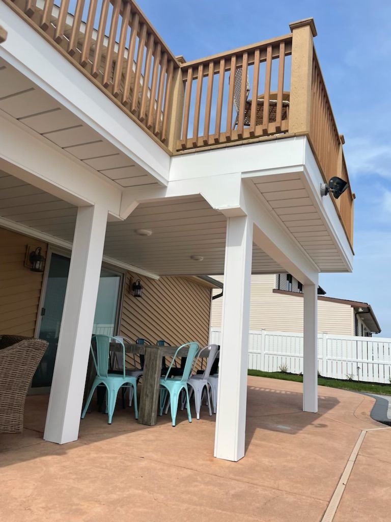 Covered patio under a wooden deck with white support posts and turquoise outdoor chairs