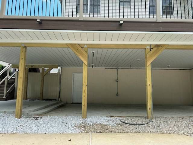 Covered parking area under a raised building with wooden support posts and gravel ground.