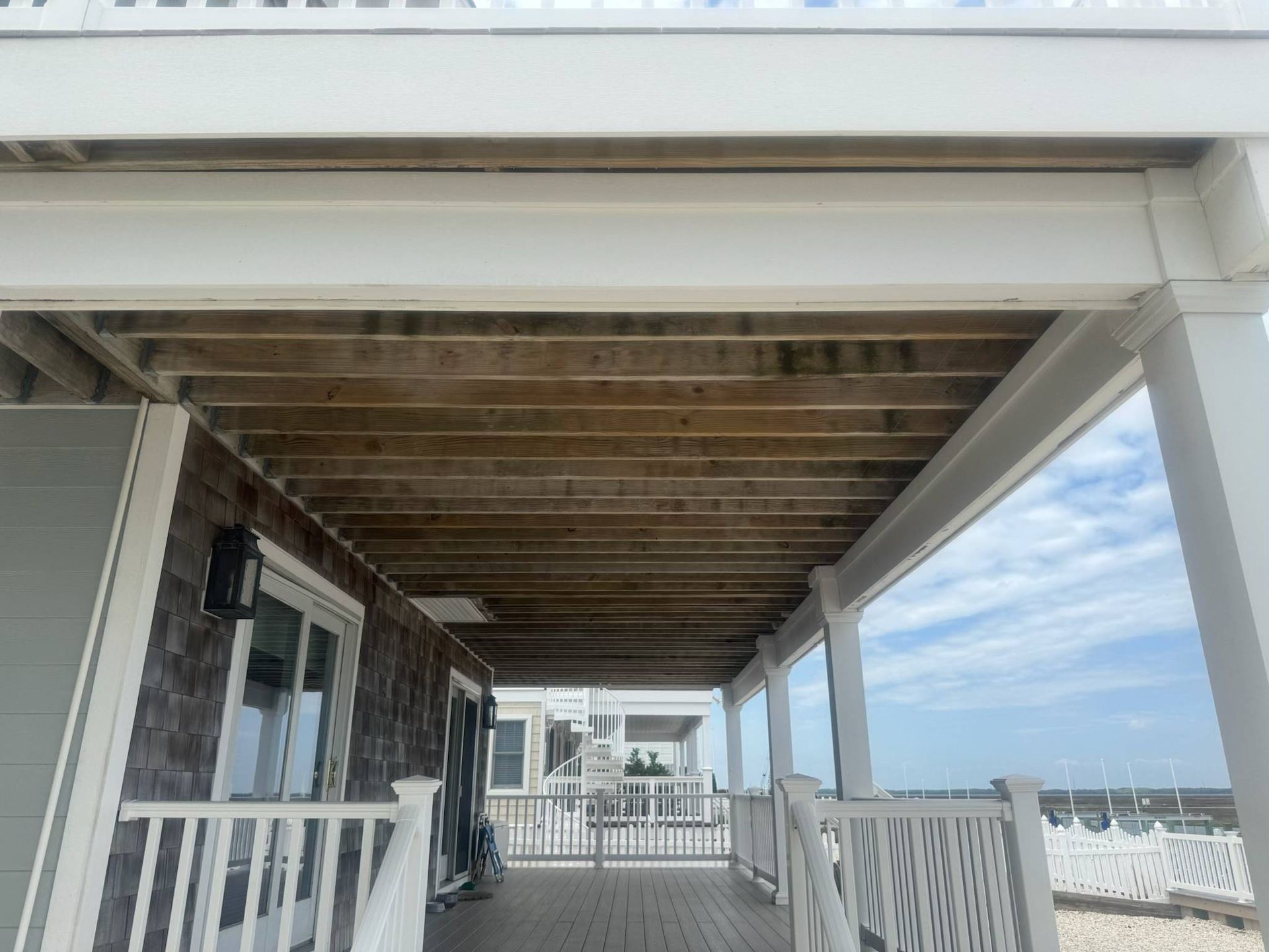 Covered seaside deck with white railings and exposed wooden beams overlooking the marina