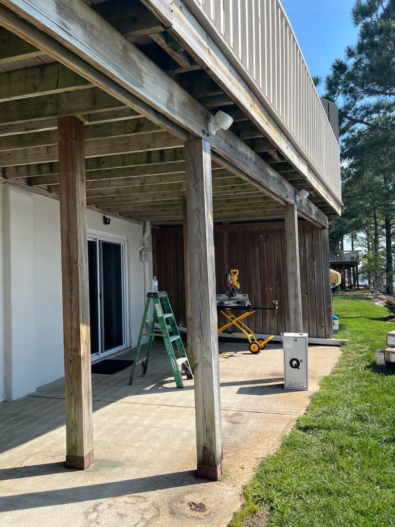 Patio under a raised deck with ladders, a table, and a grill beside a grassy yard