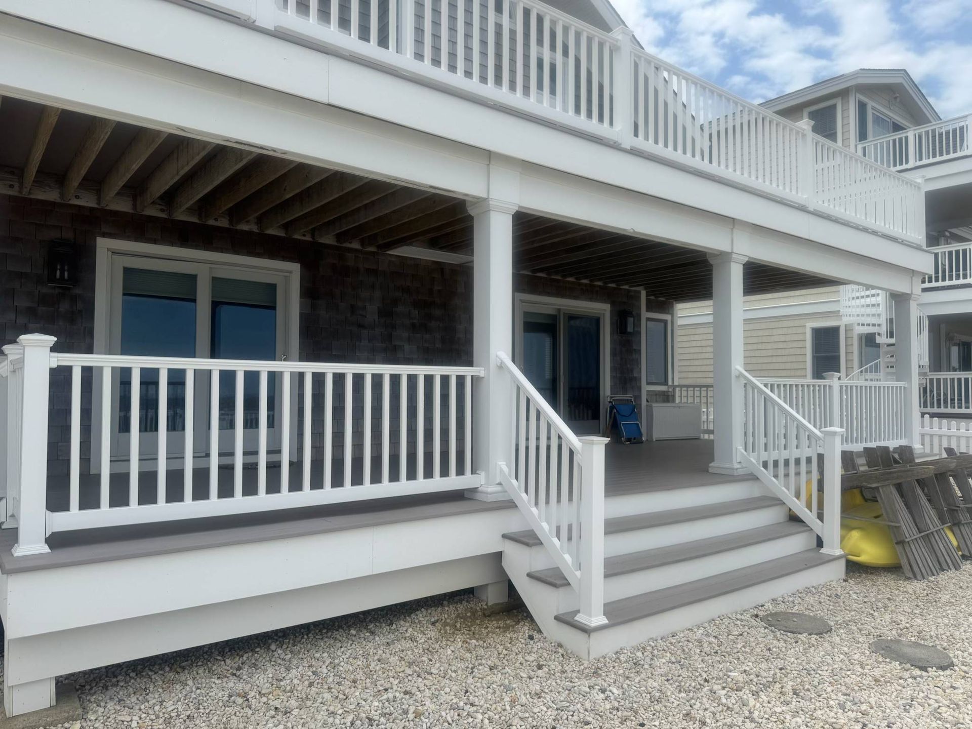 White beach house porch with stairs, railings, and blue doors on a gravel lot