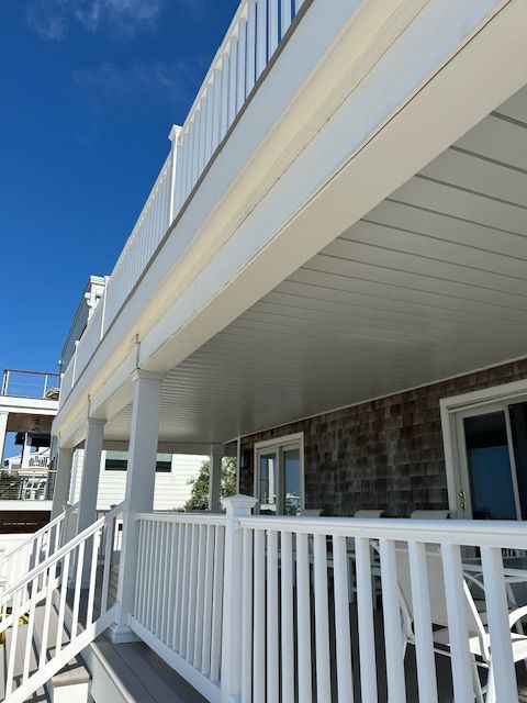 White porch with railings and columns under a blue sky beside a stone house
