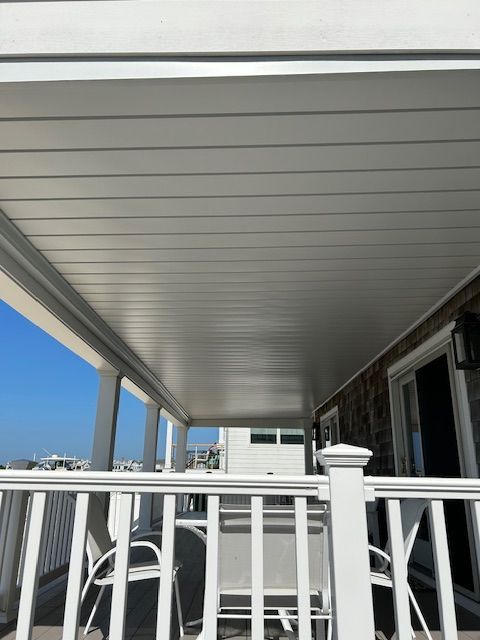 Covered porch with white railing and chairs, overlooking a bright blue sky and neighboring building.