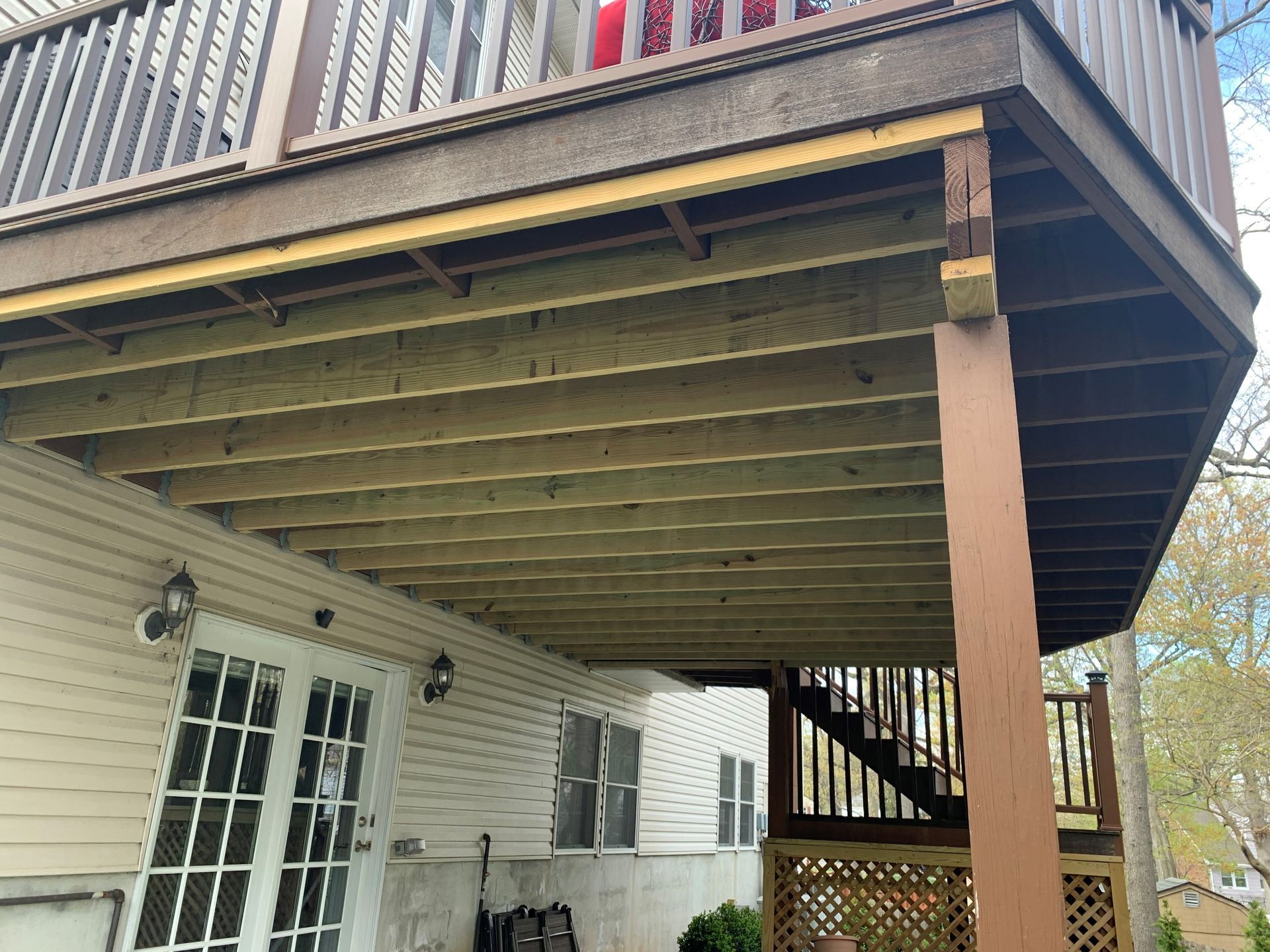 Backyard deck over a white house, with stairs and railing above a covered patio