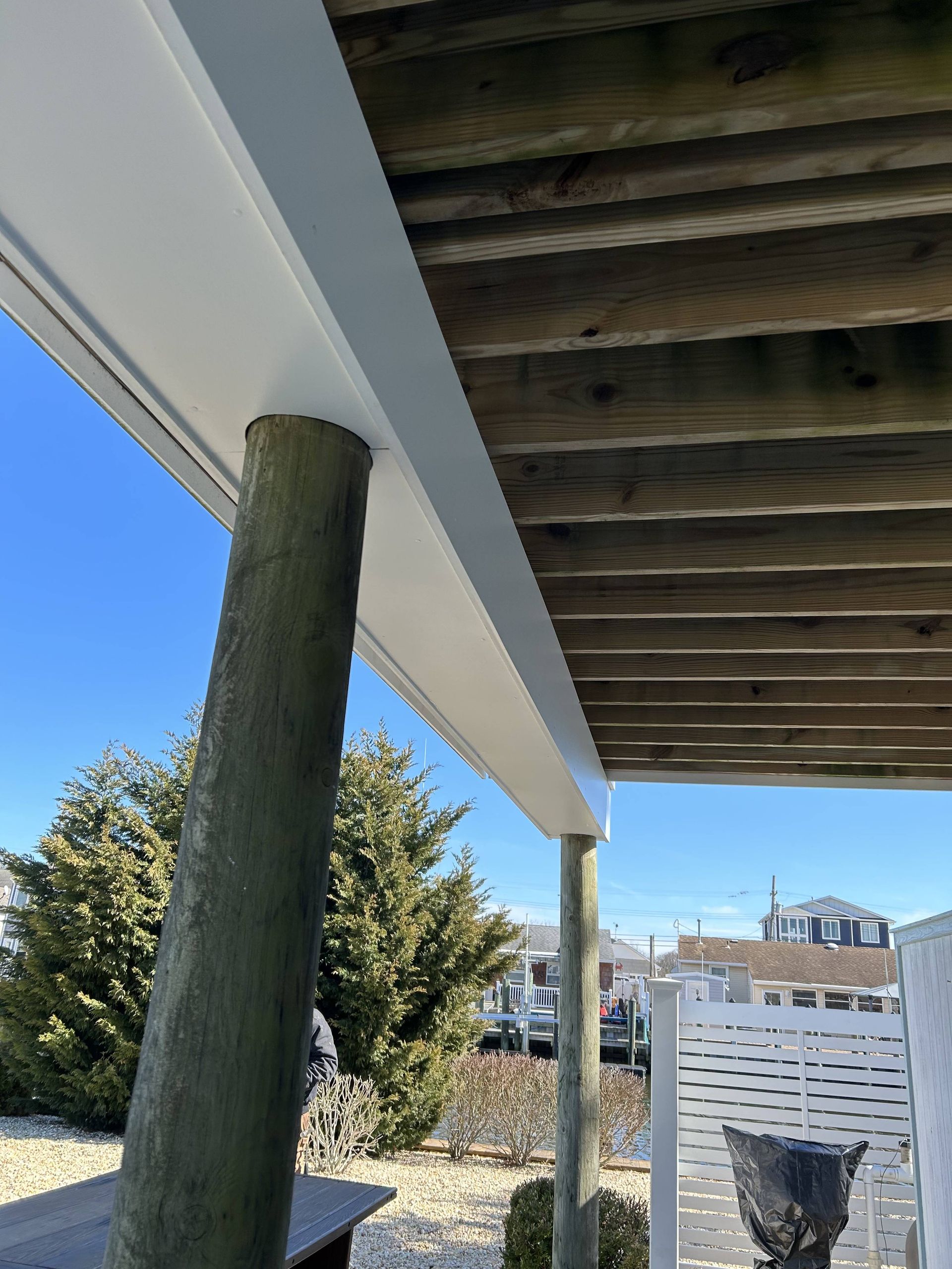 Under a deck with wooden posts, white trim, and a view of the ocean and buildings beyond