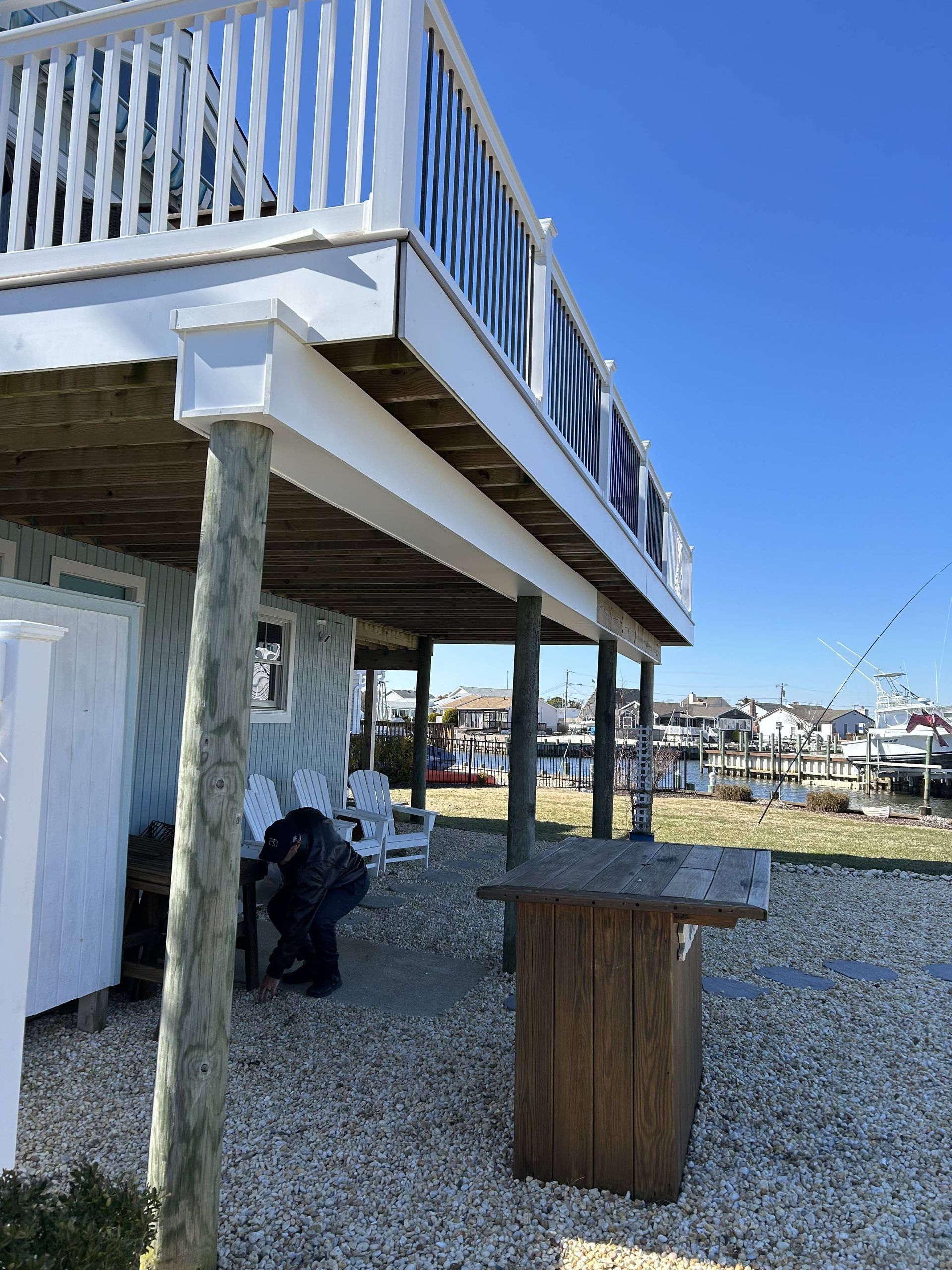 Stilted deck with white railing overlooking a gravel yard and blue sky by the waterfront