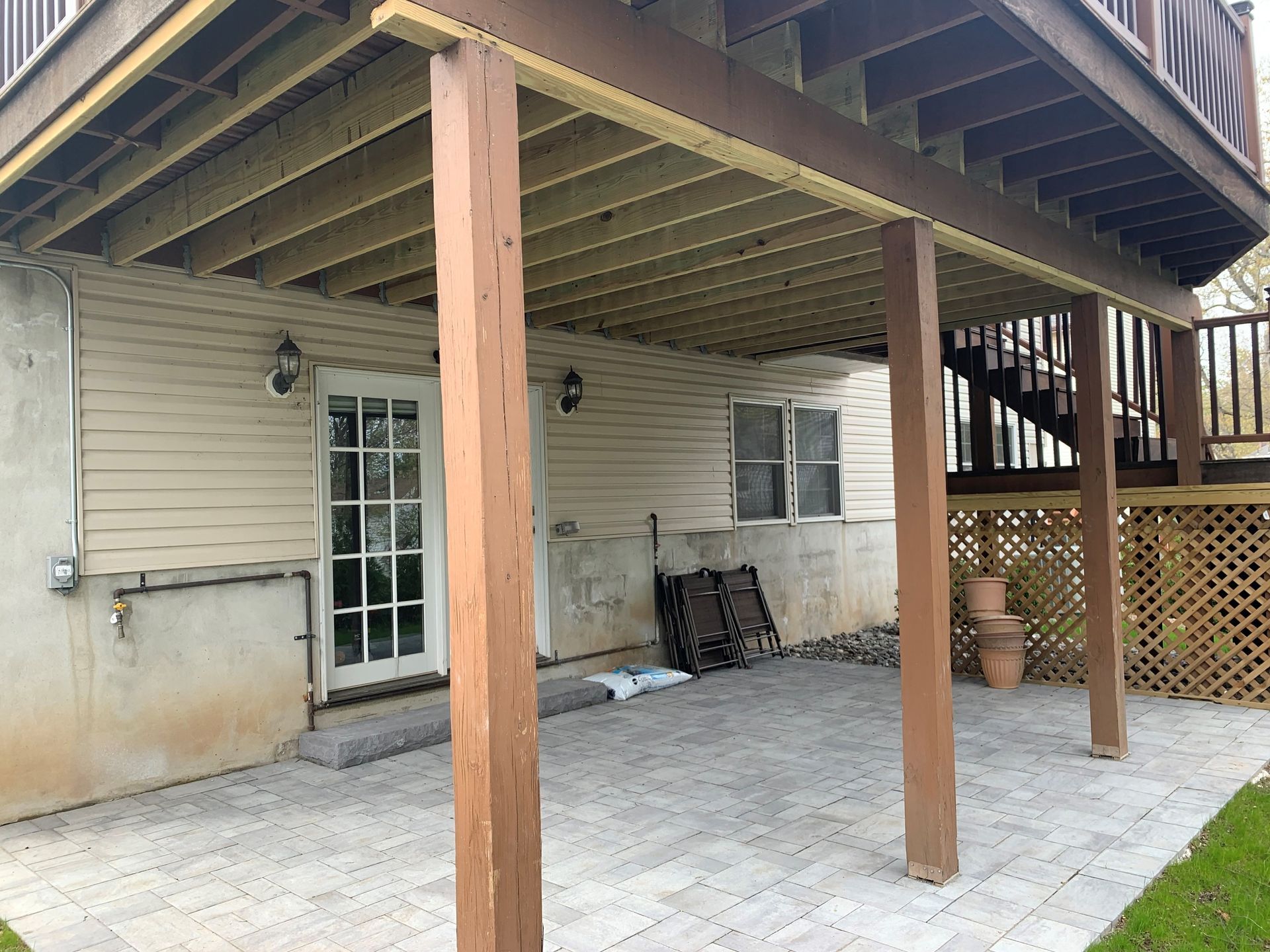 Covered backyard patio with wooden support posts, white siding, glass door, and a tiled floor