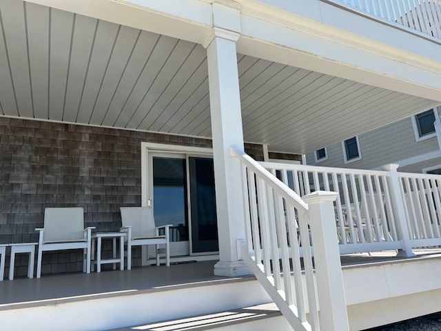 Covered porch with white railings, patio chairs, and sliding glass doors on a house exterior