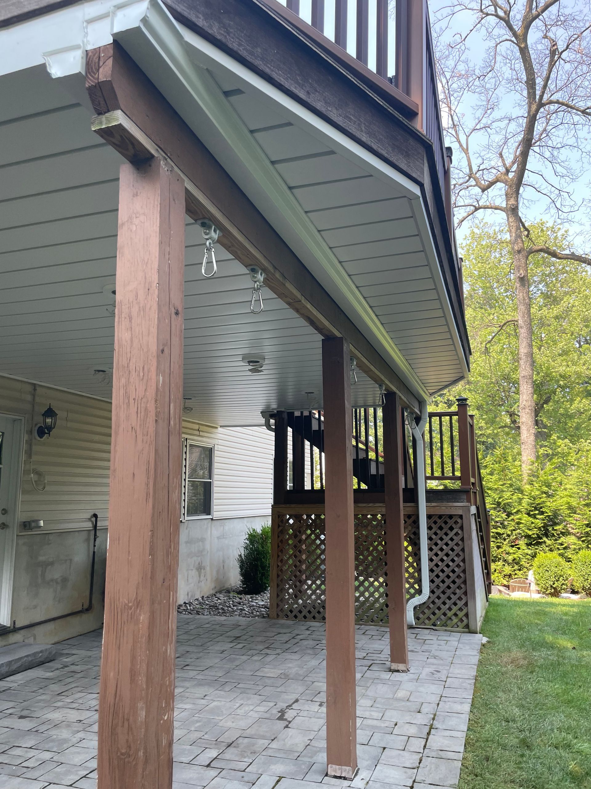 Covered wooden deck with posts, lattice skirting, and a paved patio beside a grassy yard.