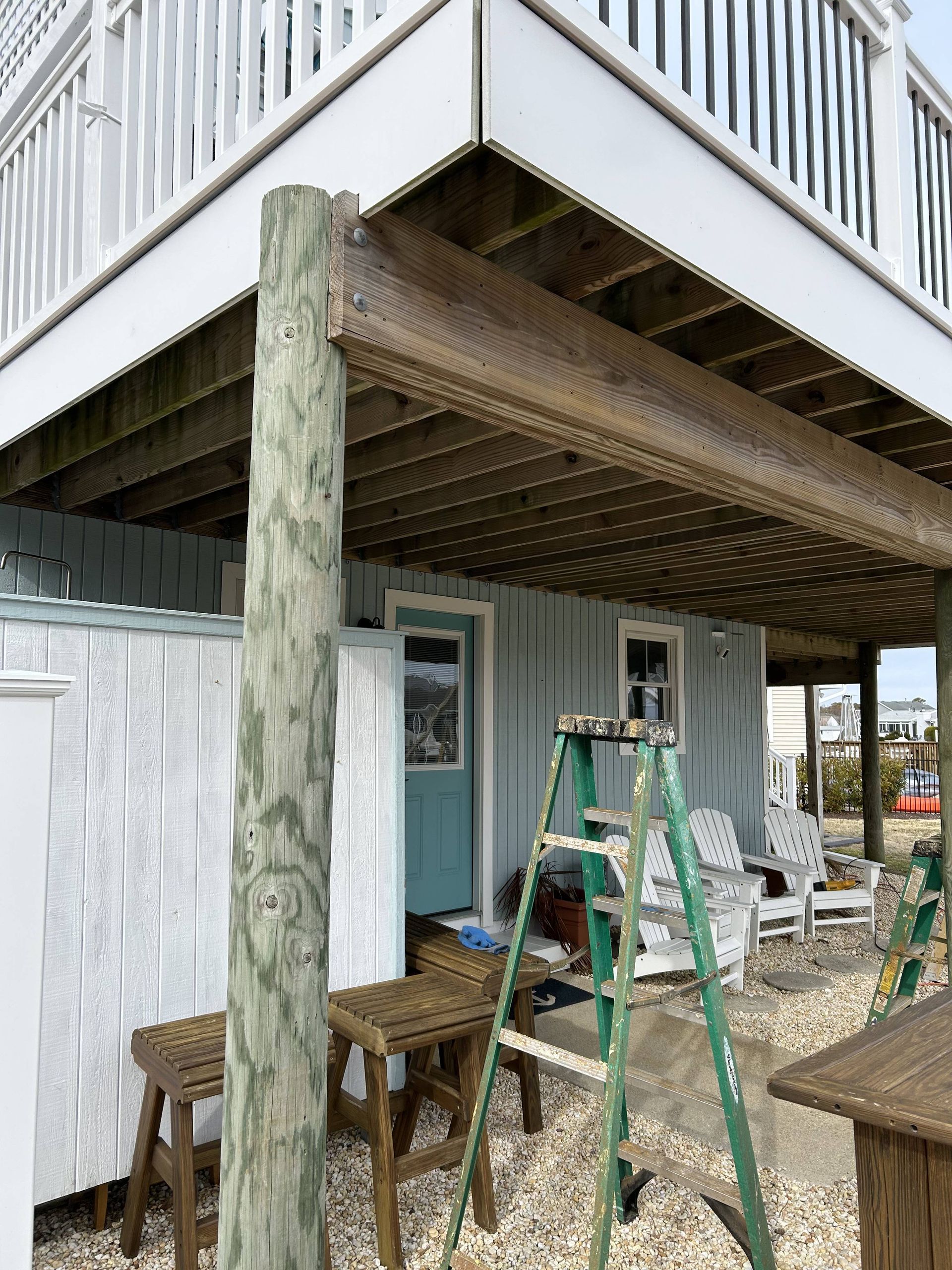Backyard deck under construction with ladders, tools, and wood supports beside a house