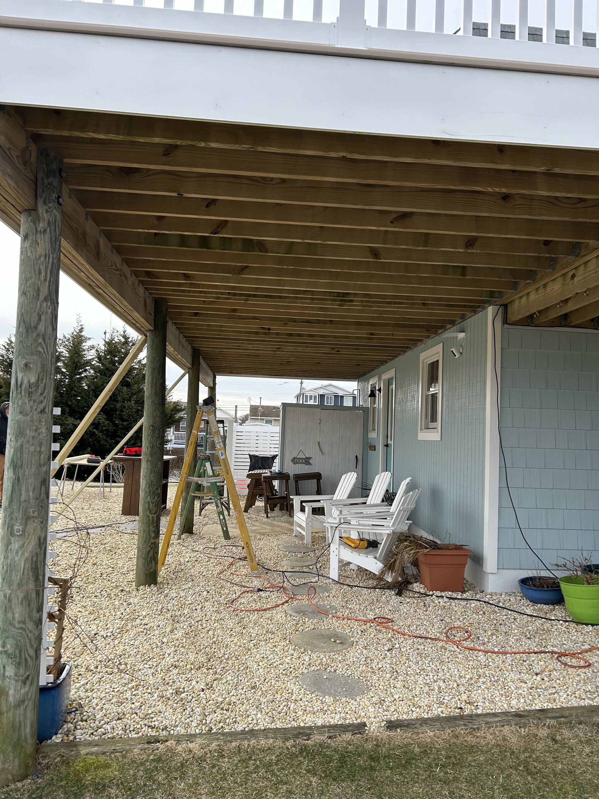Covered porch beside a mobile home with chairs, a ladder, and gravel ground under an awning