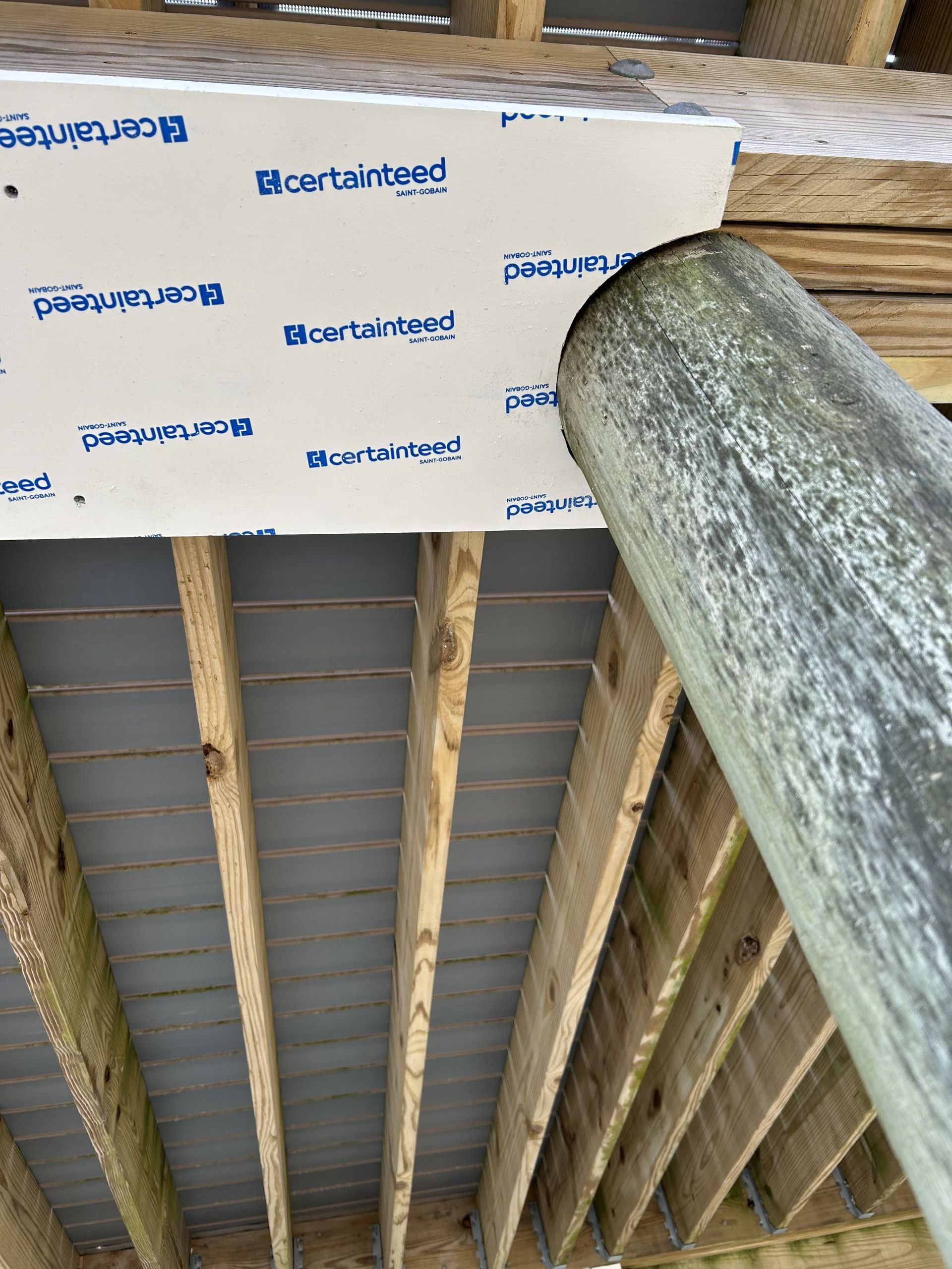 Ceiling under construction with exposed rafters, insulation panels, and a large metal support column.
