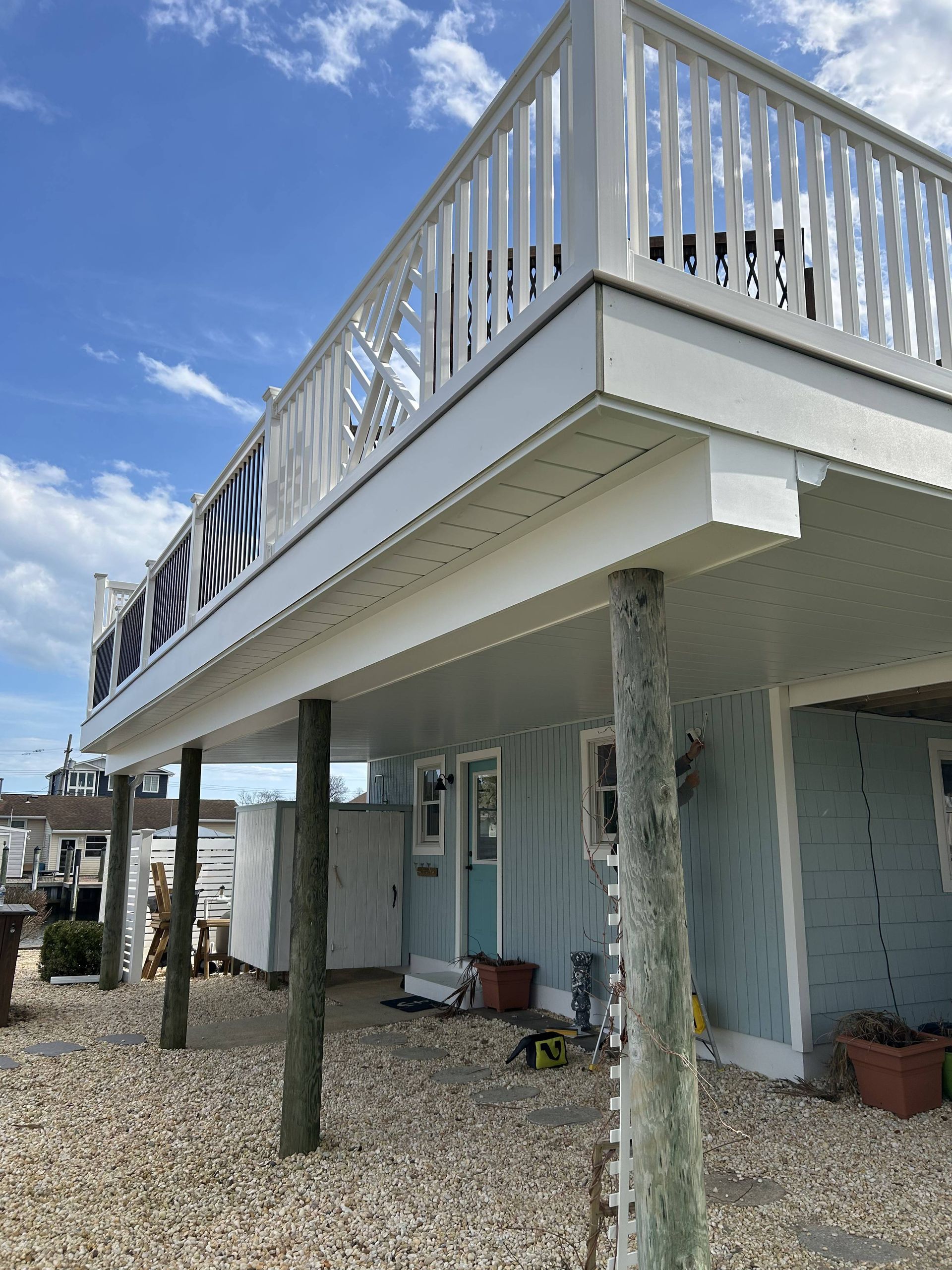 Stilted beach house with white deck railing and blue siding under a partly cloudy sky
