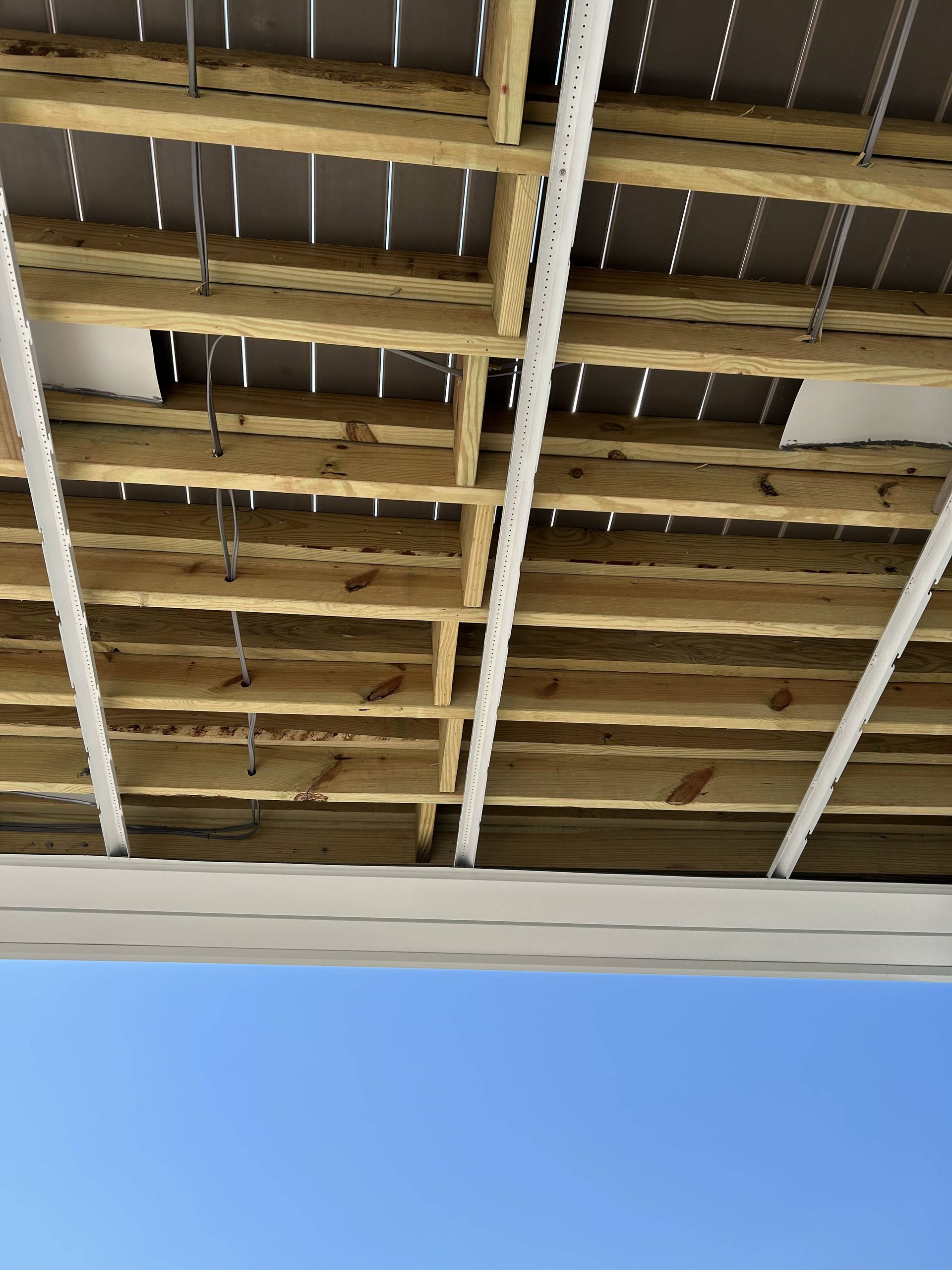 Damaged ceiling with exposed beams and hanging wires above a blue wall