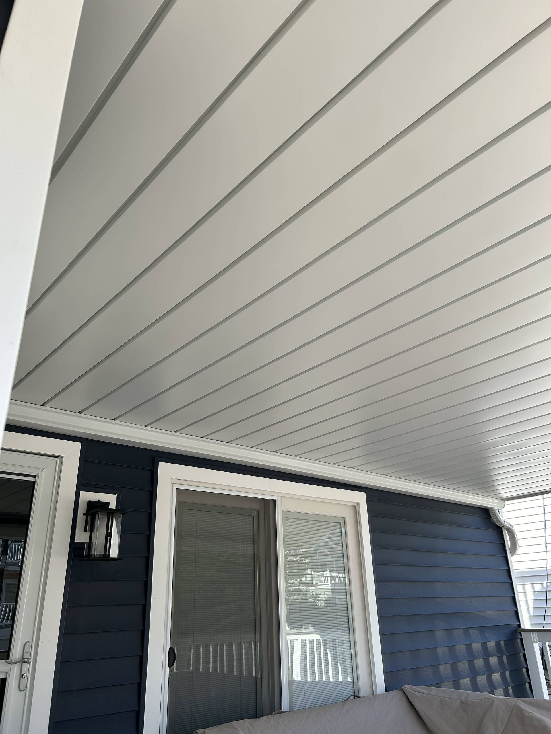 Covered porch with white ceiling, dark blue siding, and sliding glass door with blinds