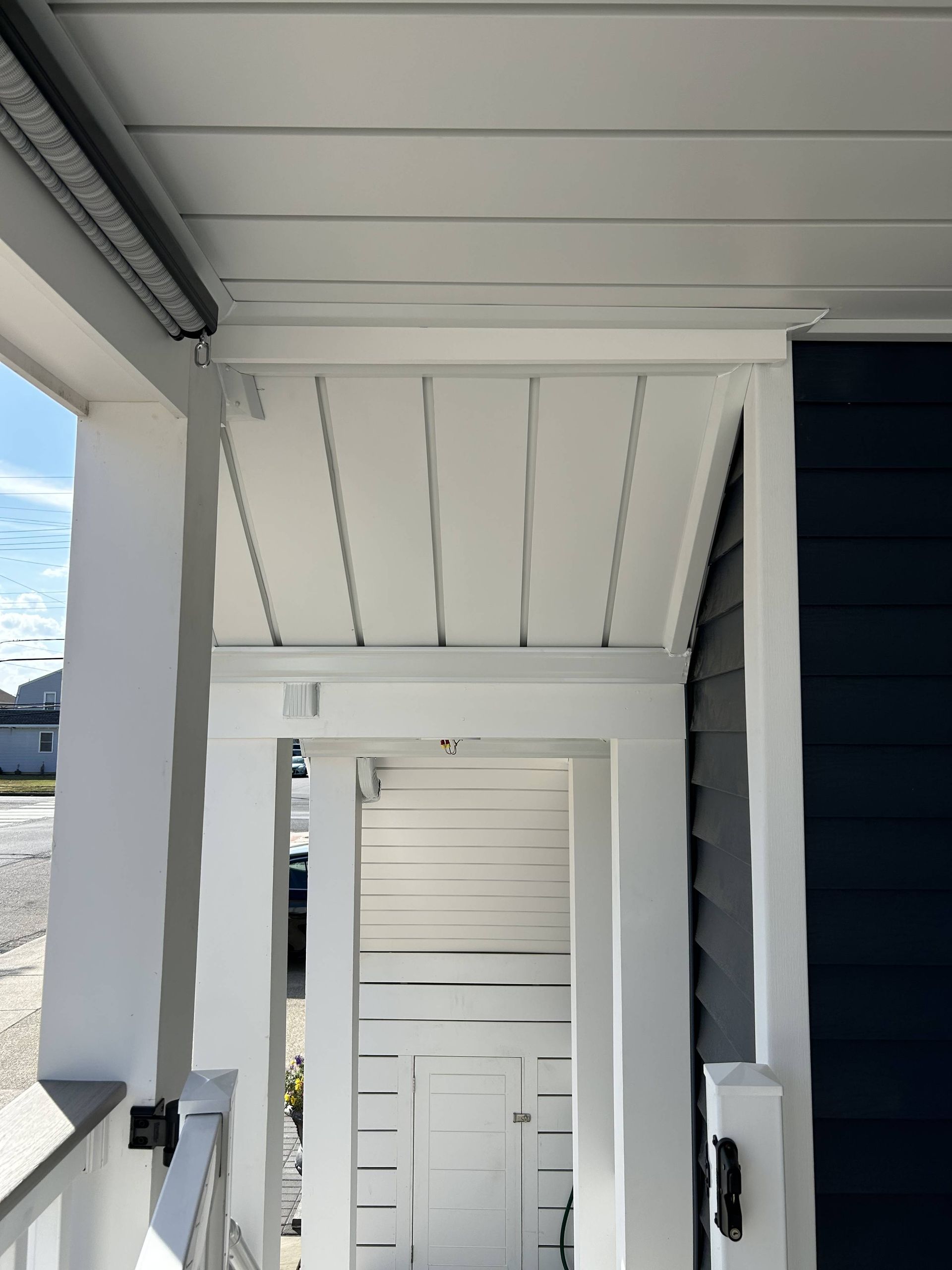 White balcony corridor with railing, ceiling beams, and a dark doorway at the end.