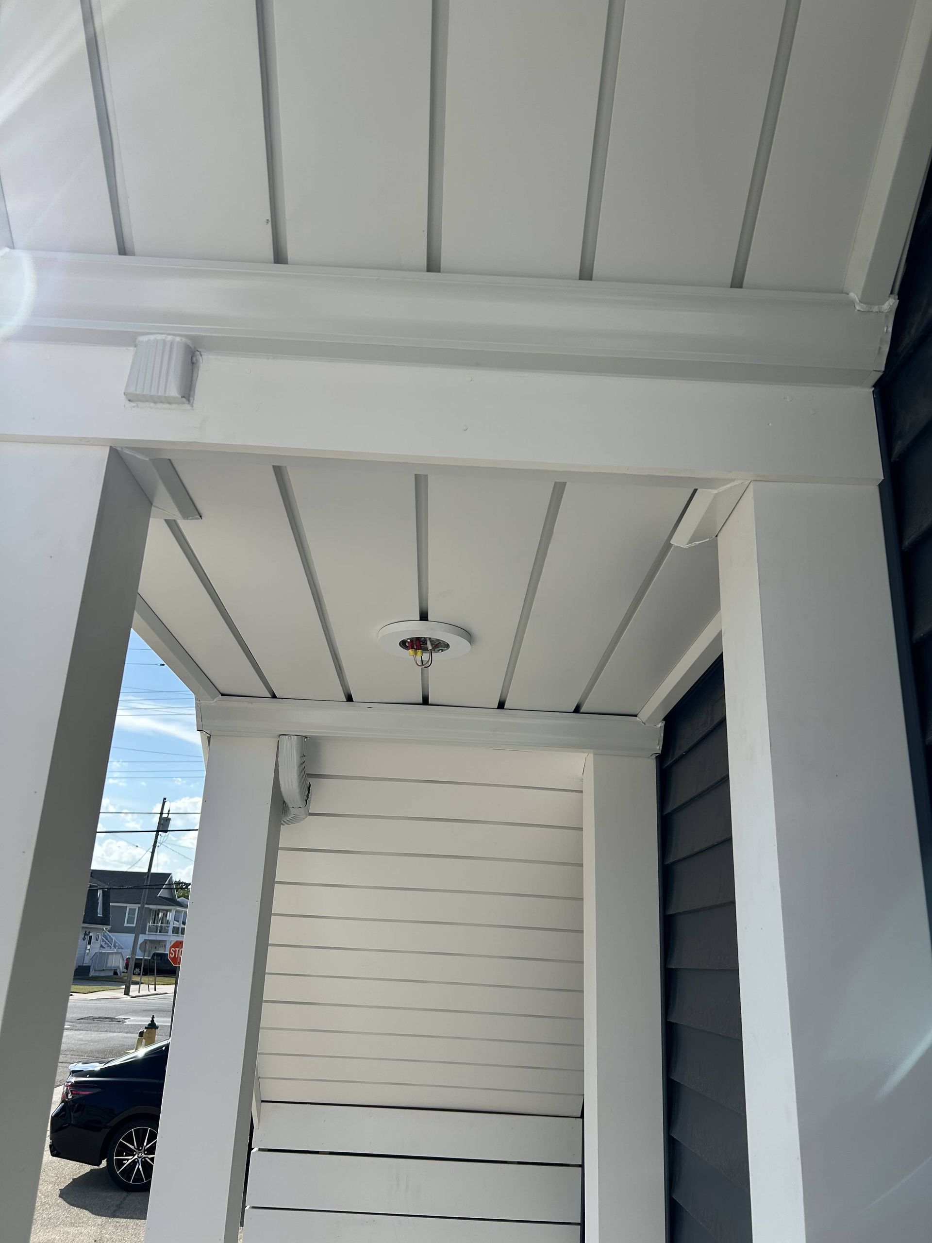 White porch ceiling and entryway with horizontal siding, framed by white columns and an outdoor light fixture.