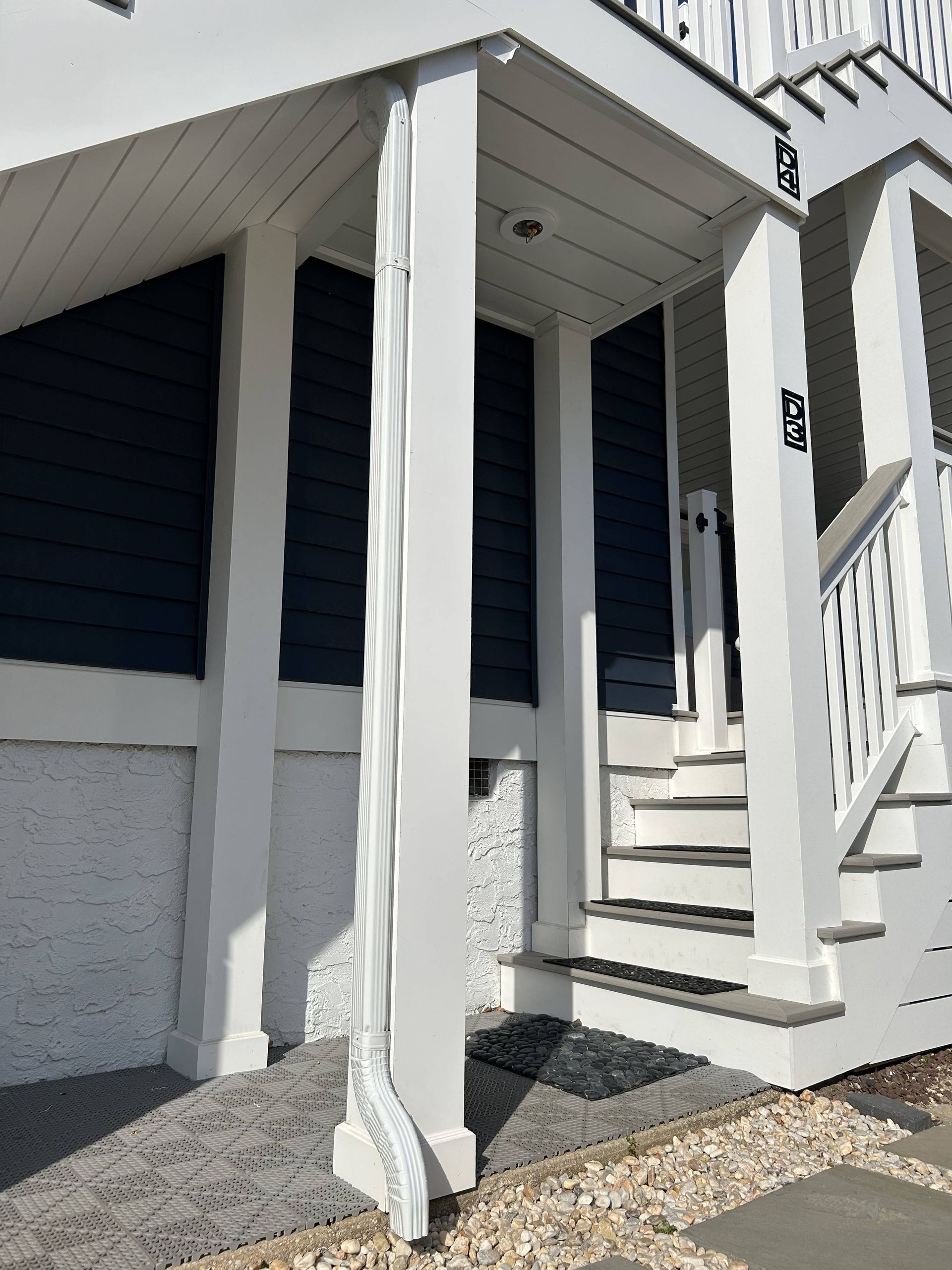 White porch entrance with stairs, railing, and navy shutters on a house exterior