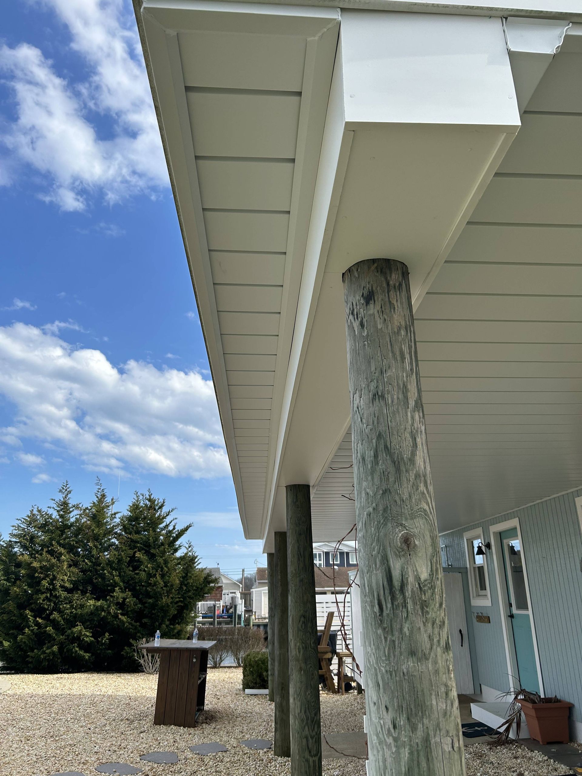 Exterior view of a coastal house with white siding, a column, and pebbled yard under a blue sky