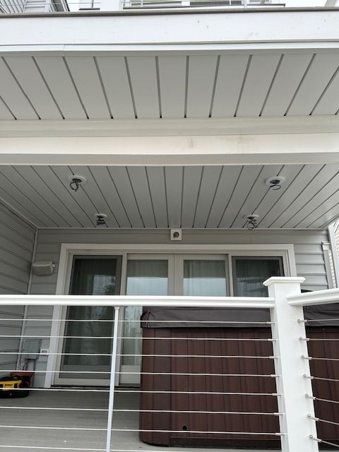 Covered balcony with gray siding, white railing, sliding glass doors, and a brown hot tub cover