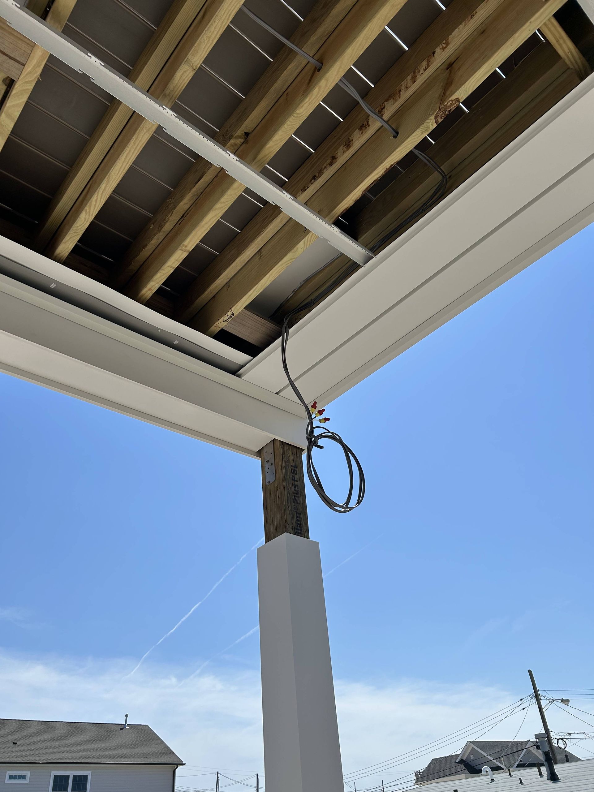 Underneath a house roof with exposed beams, a hanging cable, and blue sky above a snowy yard