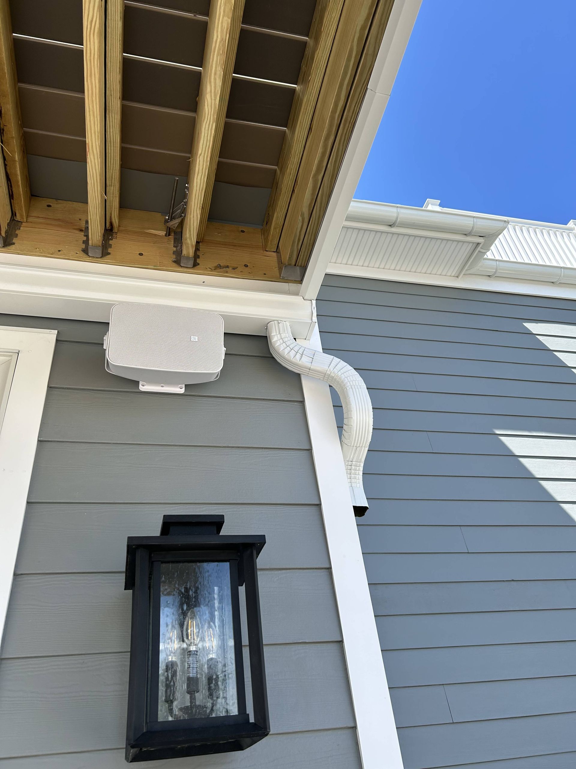 White house corner with black lantern, gutter, and roof underside against blue sky.